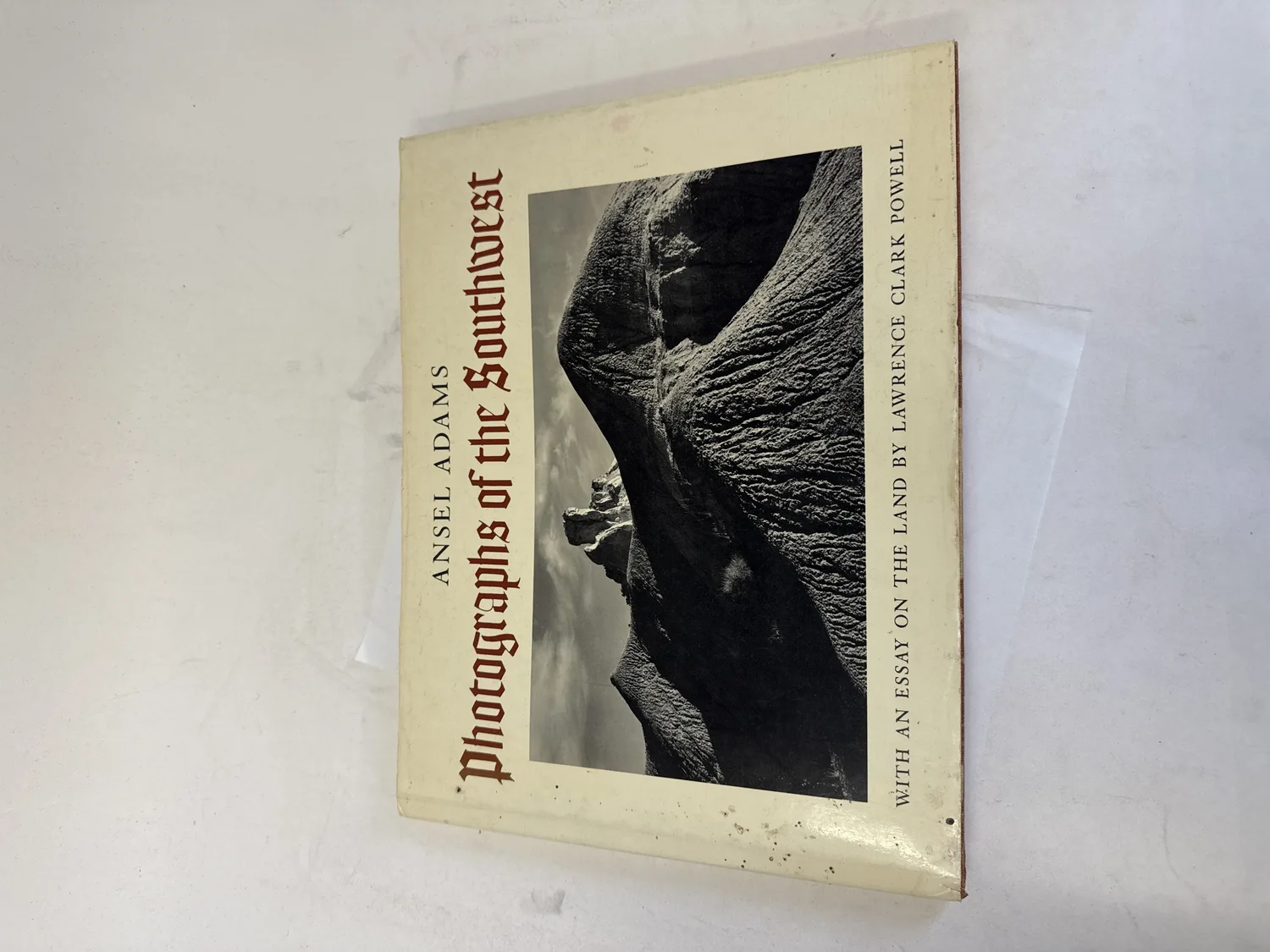 Front cover with dust jacket of Photographs of the Southwest by Ansel Adams, showing blackletter Fraktur-style typography and an Adams landscape photograph of Southwest rock formations, published by New York Graphic Society Boston 1976 with an essay on the land by Lawrence Clark Powell. Photographed at the New Mexico Literacy Project sorting desk in Albuquerque.