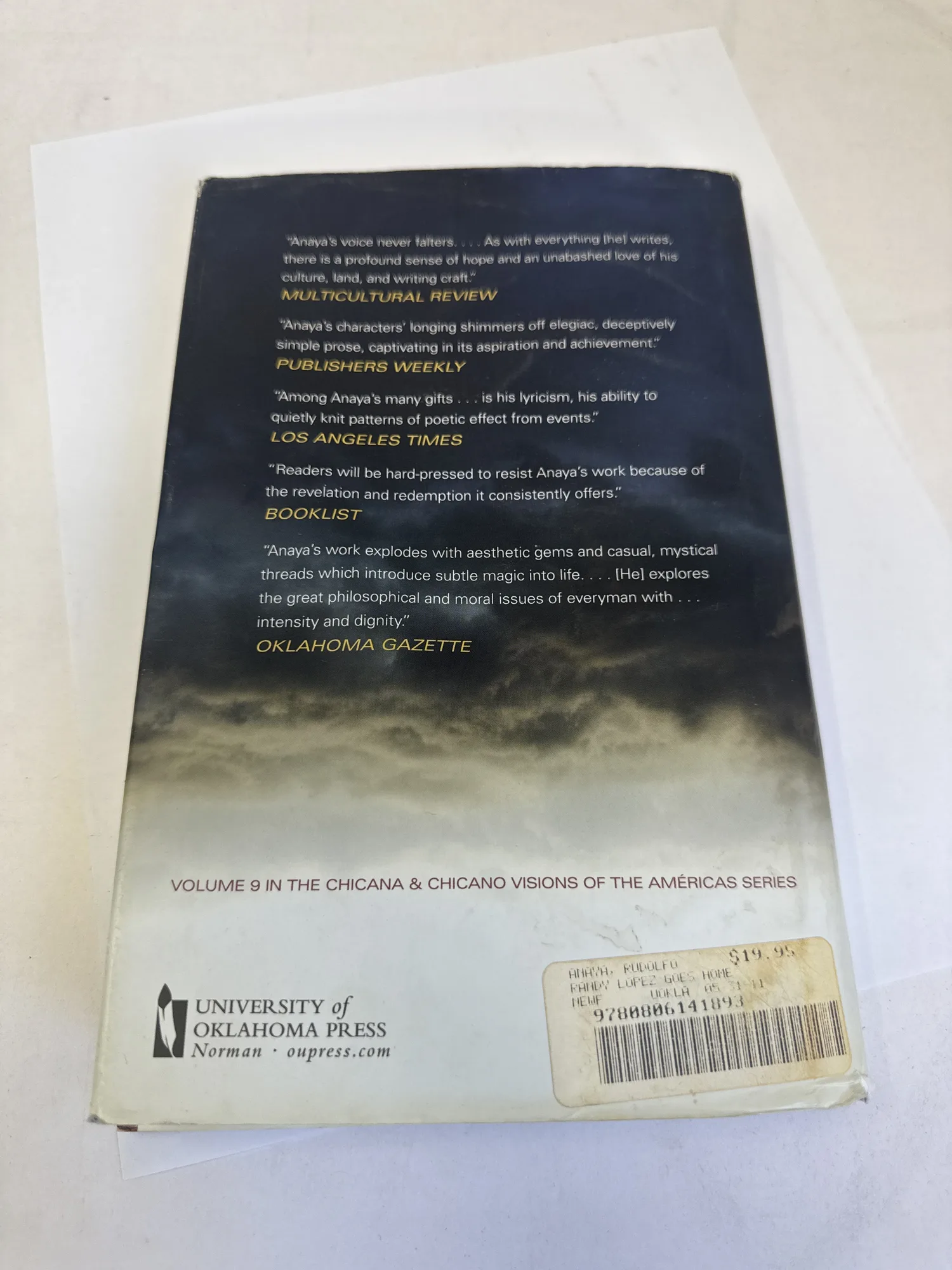 Back cover of Randy Lopez Goes Home showing review praise from Multicultural Review, Publishers Weekly, Los Angeles Times, Booklist, and Oklahoma Gazette, with University of Oklahoma Press imprint and Volume 9 in the Chicana and Chicano Visions of the Americas series designation. Photographed at the New Mexico Literacy Project sorting desk in Albuquerque.