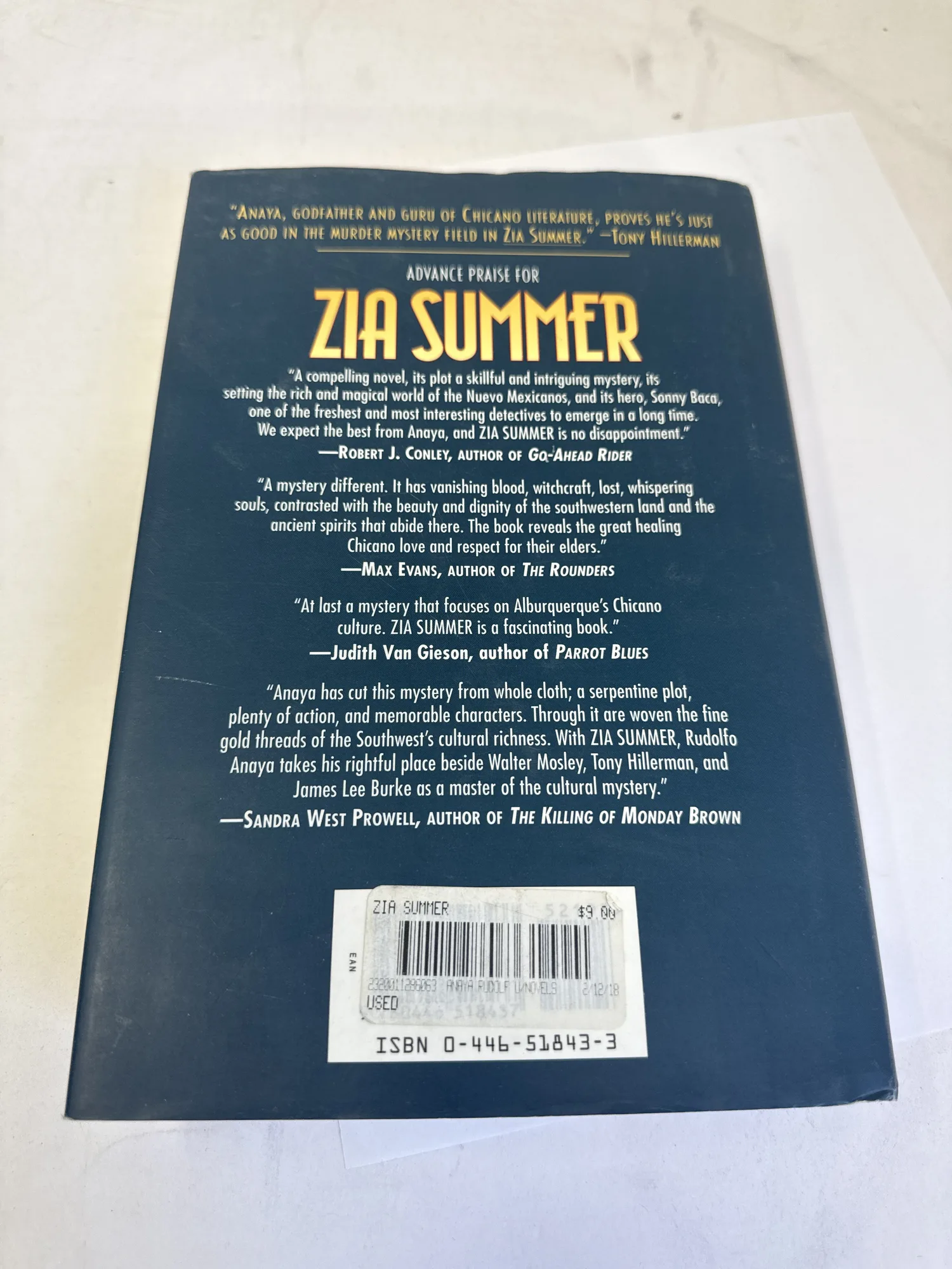 Back cover of Zia Summer by Rudolfo Anaya showing advance praise blurbs from Tony Hillerman, Robert J. Conley, Max Evans, Judith Van Gieson, James Lee Burke, and Sandra West Prowell. Photographed at the New Mexico Literacy Project sorting desk in Albuquerque.
