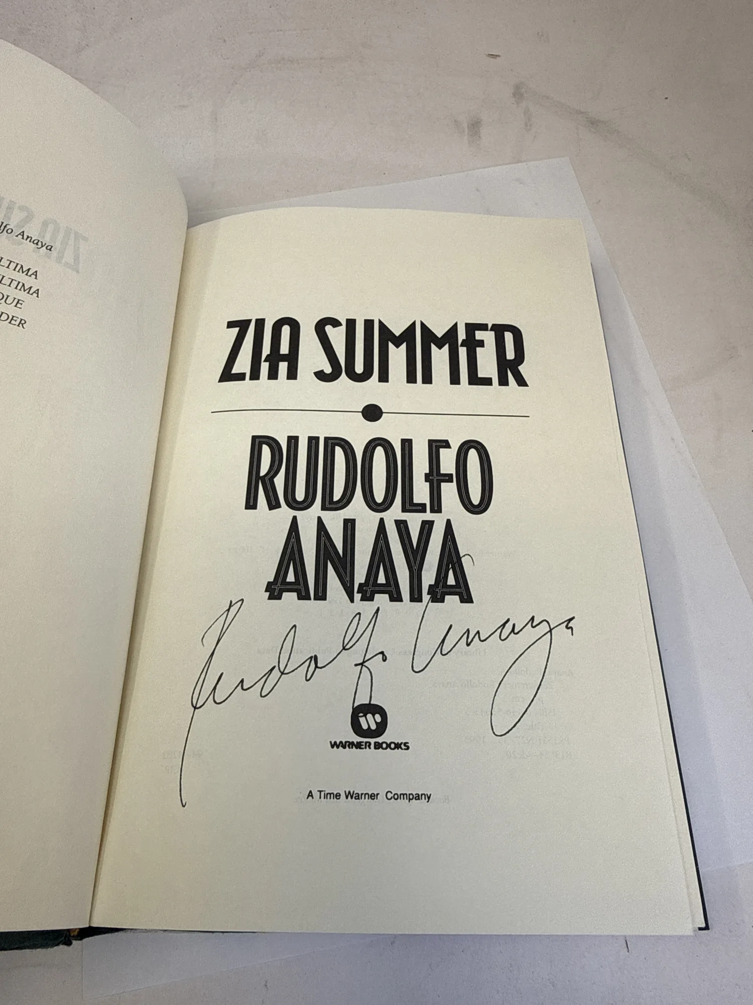 Signed title page of Zia Summer by Rudolfo Anaya, Warner Books first edition 1995, showing Anaya's bold ink signature below the Warner Books imprint. Photographed at the New Mexico Literacy Project sorting desk in Albuquerque.