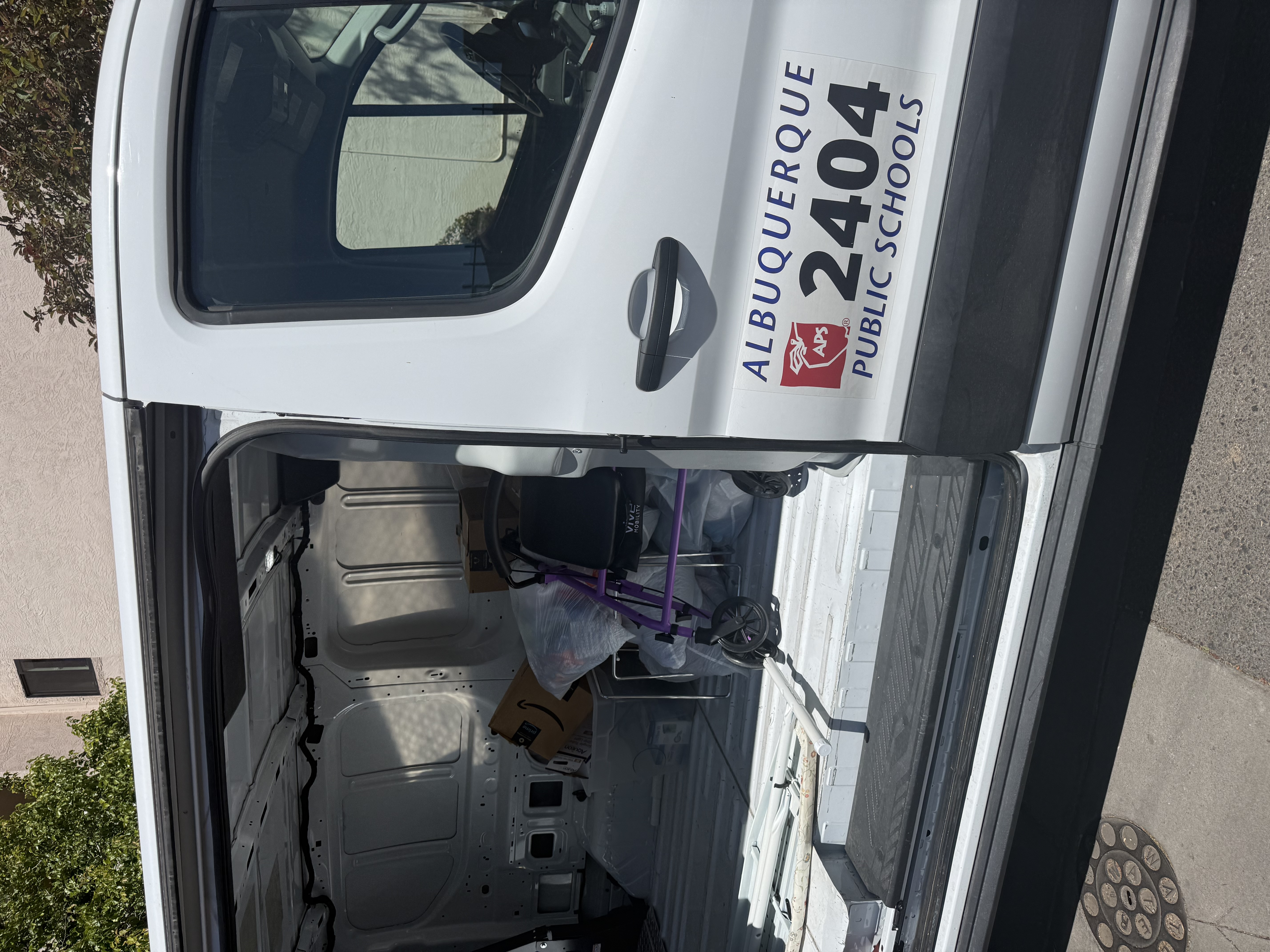 An APS Title I van with the bus number 2404 visible, parked at the NMLP warehouse on a Tuesday delivery for the McKinney-Vento program.