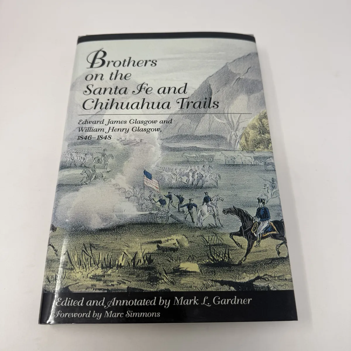 Hardcover dust jacket of Brothers on the Santa Fe and Chihuahua Trails with elegant script title and a 19th-century color lithograph of cavalry skirmish around a Mexican flag in the high desert mountains.