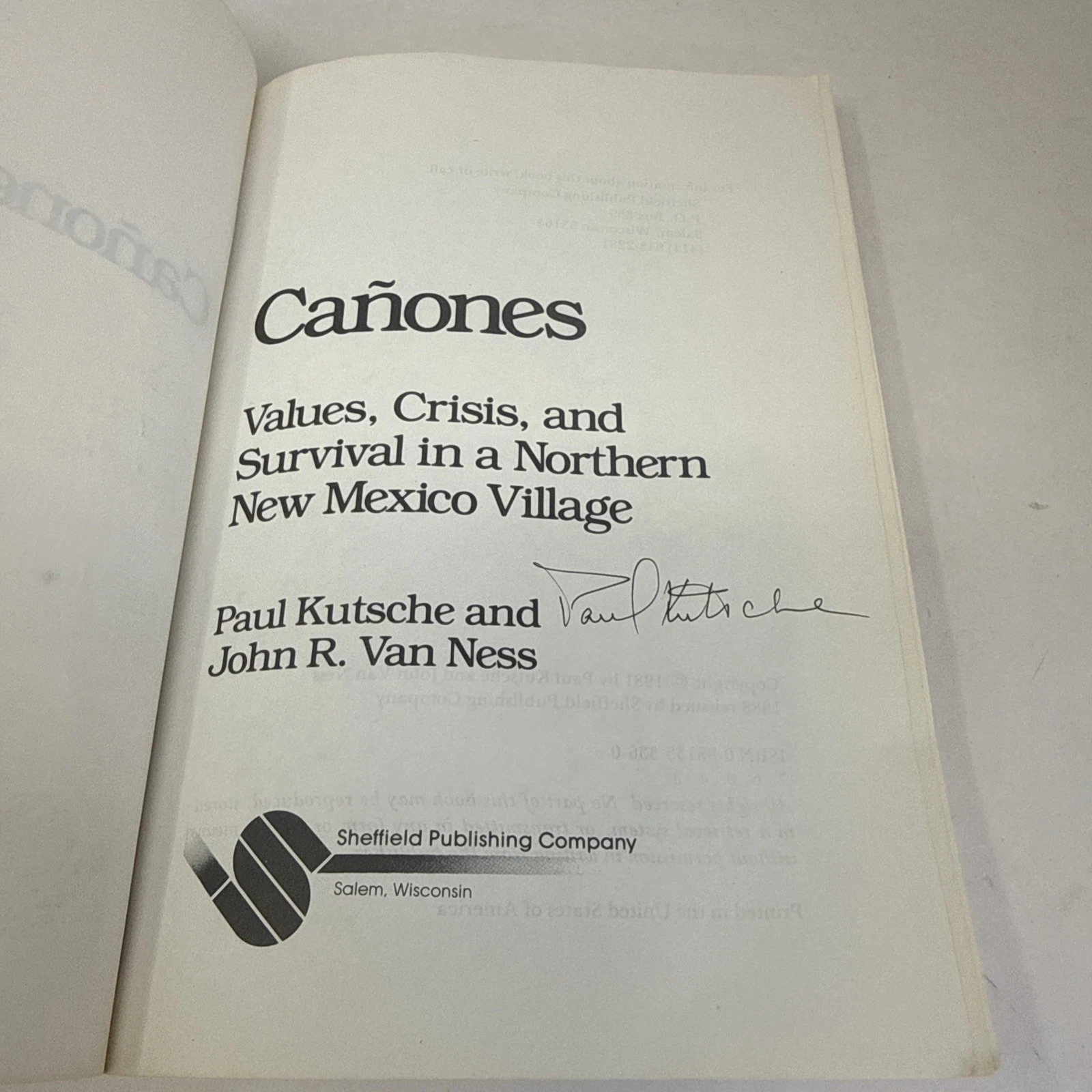 The title page of the Sheffield Publishing 1988 paperback reissue of Cañones with the signature 'Paul Kutsche' written in dark ink across the area above the byline 'PAUL KUTSCHE and JOHN R. VAN NESS'. The title 'CAÑONES: Values, Crisis, and Survival in a Northern New Mexico Village' is set in serif display capitals above the signature; the Sheffield Publishing imprint is set at the foot of the page.