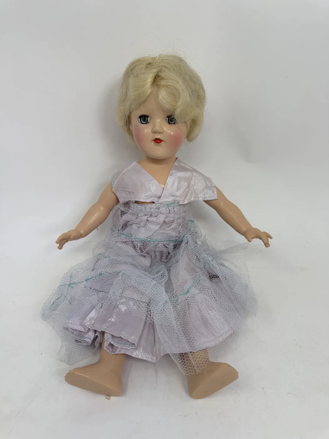 A 14-inch Ideal Toy Co. hard-plastic Toni doll standing in a pale lavender taffeta and tulle party dress, with a platinum-blonde nylon wig in a side-parted short bob, blue sleep eyes, pink cheeks, and small red painted lips