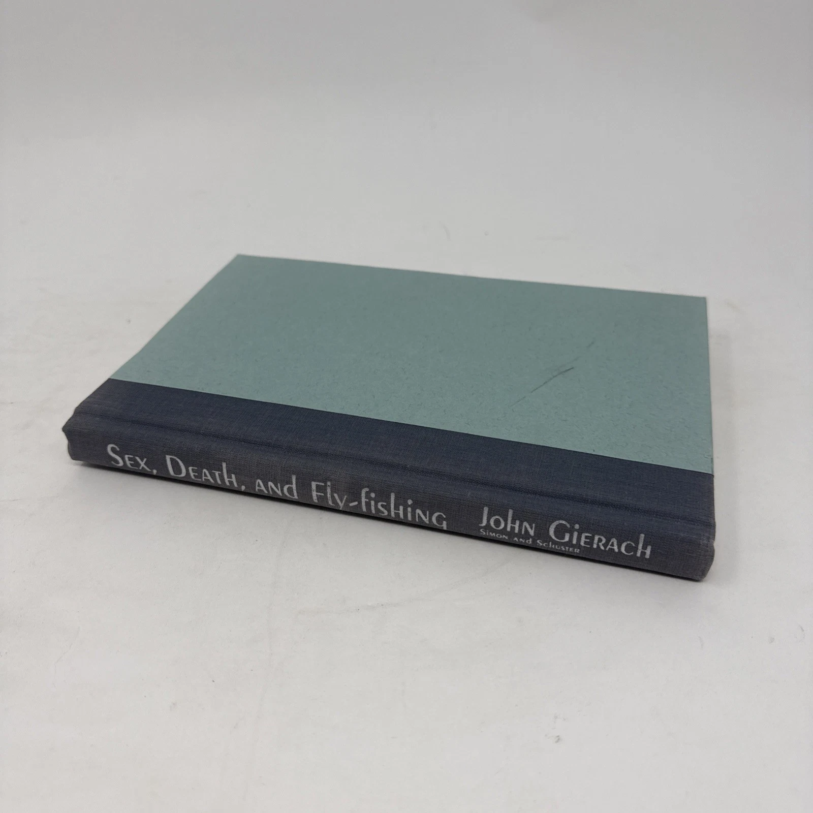 The spine of Sex, Death, and Fly-Fishing by John Gierach, Simon and Schuster hardcover, with two-tone teal cloth and dark-blue cloth back