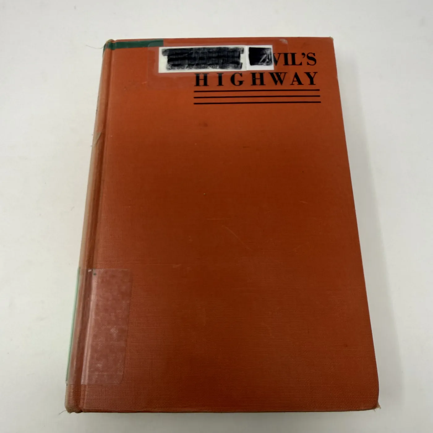 The front cover of The Devil's Highway by Richard A. Summers, bound in deep terracotta-red book cloth with the title 'VIL'S HIGHWAY' partly obscured by a thick black redaction bar where the Albuquerque Public Library has covered the original publisher's stenciled title block; black double-rule below the title; lower edge of the cover plain. A small remnant of a green book-cloth library reinforcement strip is visible at the bottom-left corner where the spine wraps onto the front board.