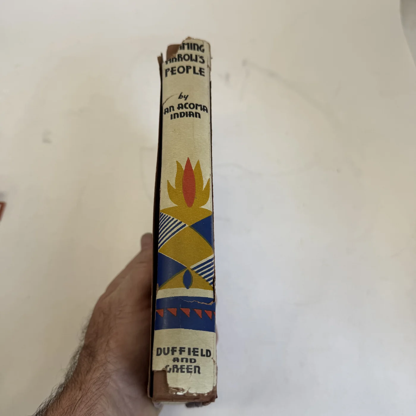 The dust-jacket spine of Flaming Arrow's People: title, the byline 'by AN ACOMA INDIAN', a tall flame-and-diamond Pueblo motif in yellow, red and blue, and 'DUFFIELD and GREEN' at the foot; chips at the head and along the folds.