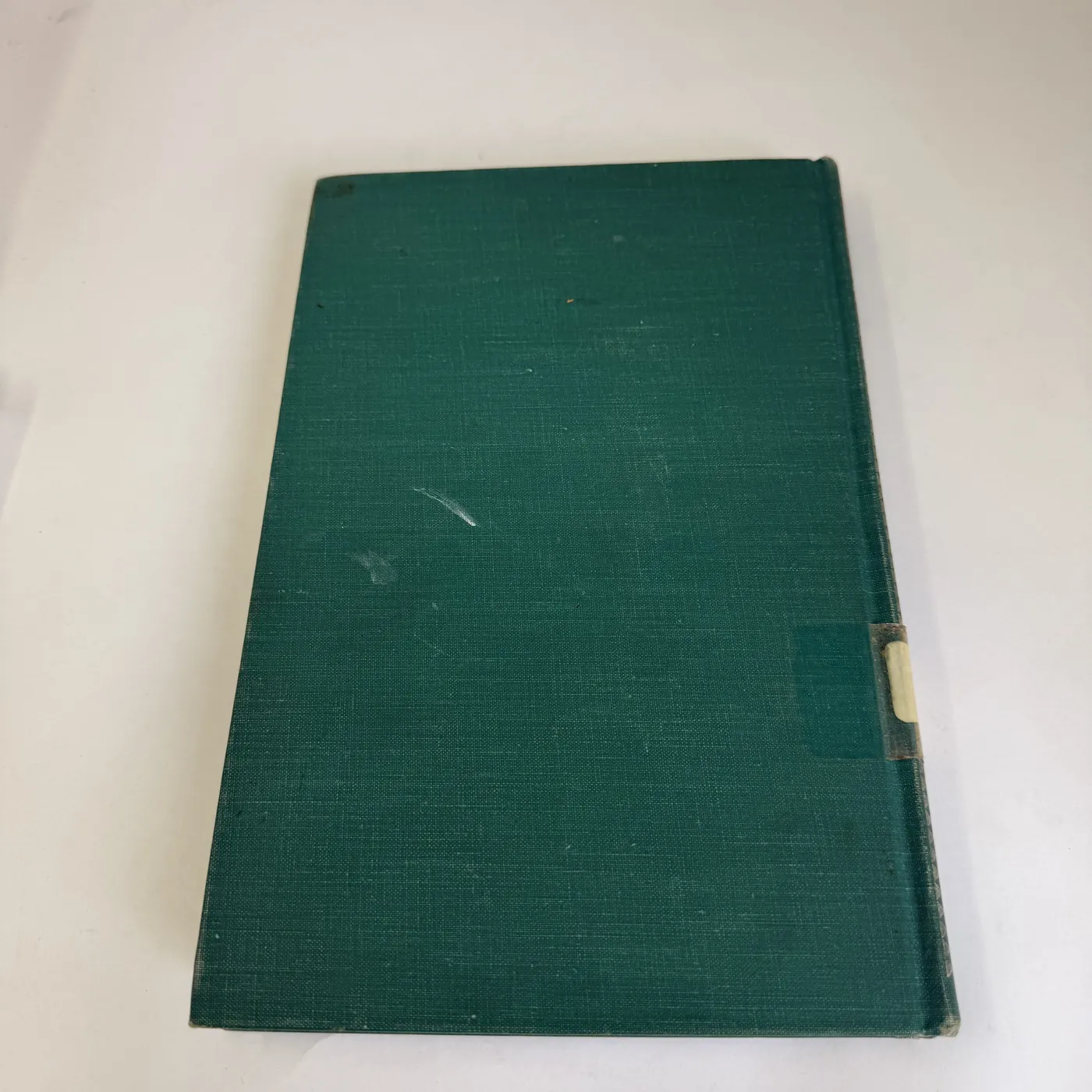 The back cover of the book, plain dark green book-cloth identical to the front cover, with no surface lettering. A small remnant of what was once an Albuquerque Public Library patron-circulation pocket is visible along the right edge near the spine, partly torn away when the book was withdrawn from circulation.