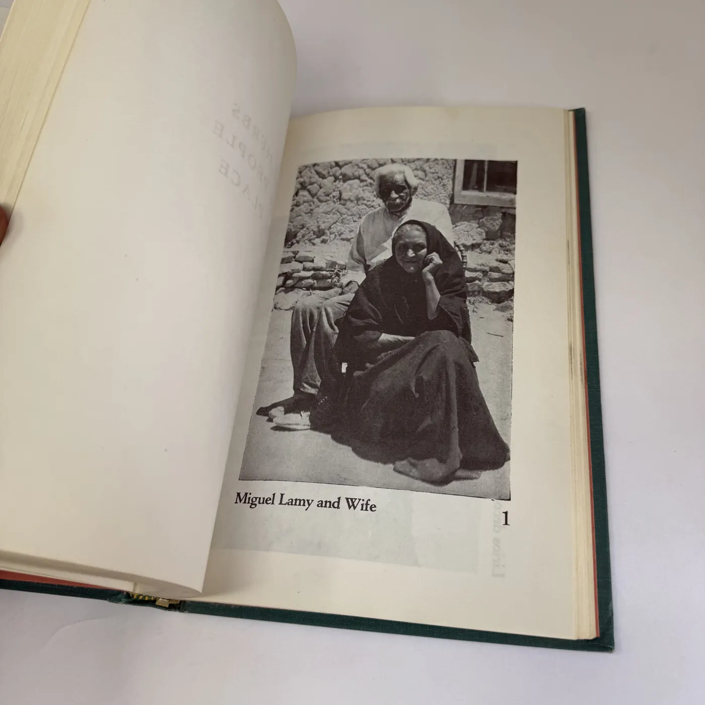 The frontispiece photograph at page 1 of the book, showing a sepia-toned period photograph of an elderly Spanish New Mexican man (Miguel Lamy) sitting on a stone bench against the adobe wall of a village house with his wife seated beside him in a long dark shawl, both looking off-camera. The caption beneath reads: 'Miguel Lamy and Wife.'