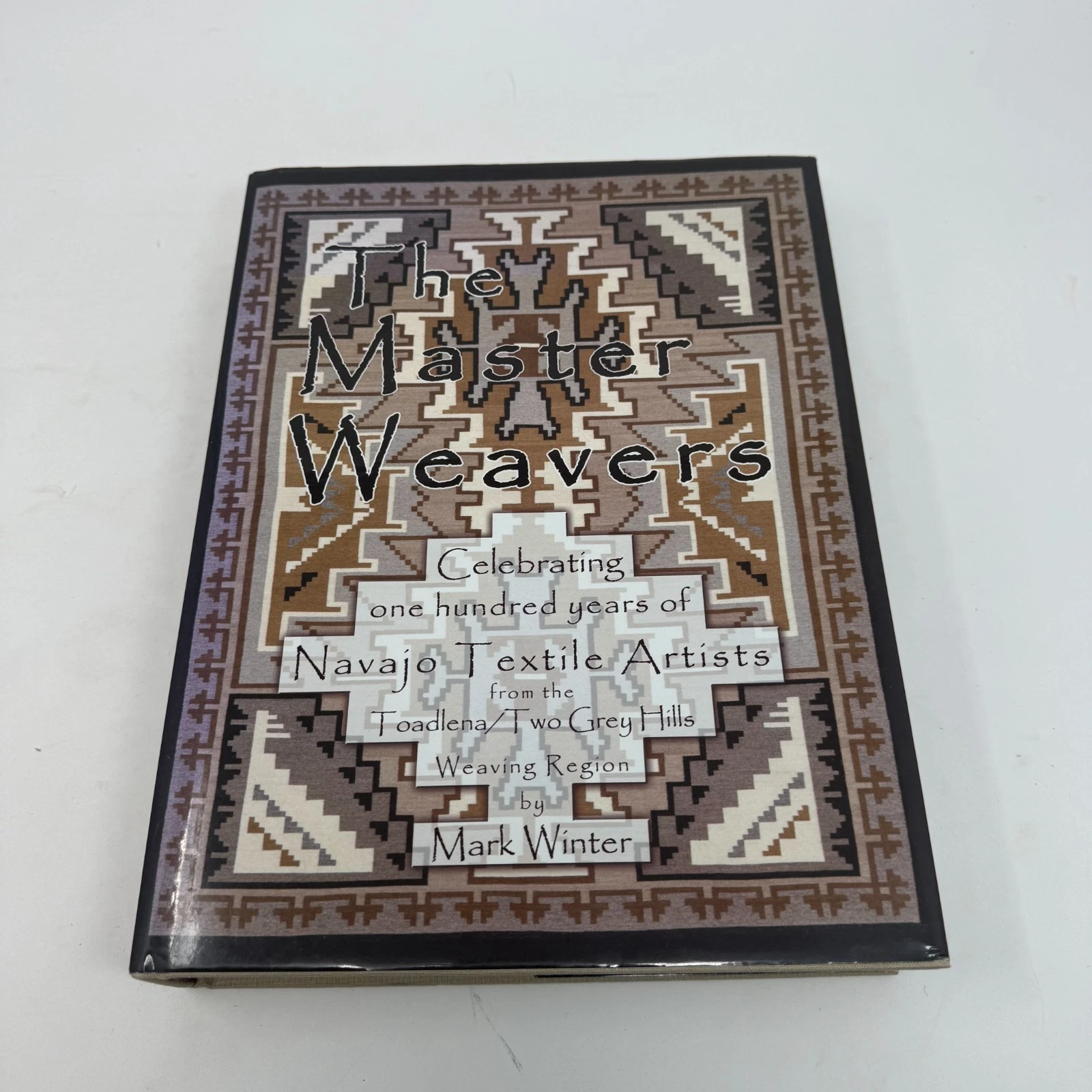 The dust jacket of The Master Weavers by Mark Winter, with a Two Grey Hills Navajo rug pattern in the central illustration framed by additional weaving motifs.