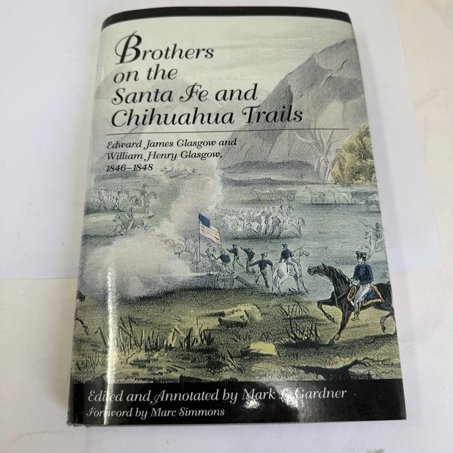 Front cover with dust jacket of Brothers on the Santa Fe and Chihuahua Trails by Edward James Glasgow and William Henry Glasgow 1846-1848, edited by Mark L. Gardner, foreword by Marc Simmons, University Press of Colorado 1993 first edition, dust jacket showing Mexican War battle scene engraving with mounted cavalry, infantry carrying American flag, and cannon smoke against a mountain backdrop, photographed at New Mexico Literacy Project workspace in Albuquerque