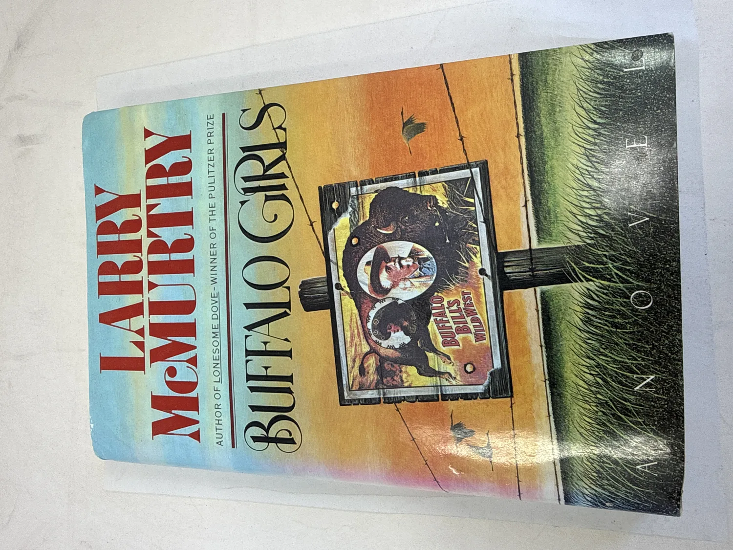 Front cover of Buffalo Girls by Larry McMurtry, first edition 1990 Simon and Schuster, showing Wild West show illustration with buffalo imagery. Author credited as winner of the Pulitzer Prize for Lonesome Dove. Photographed at the New Mexico Literacy Project sorting desk in Albuquerque.