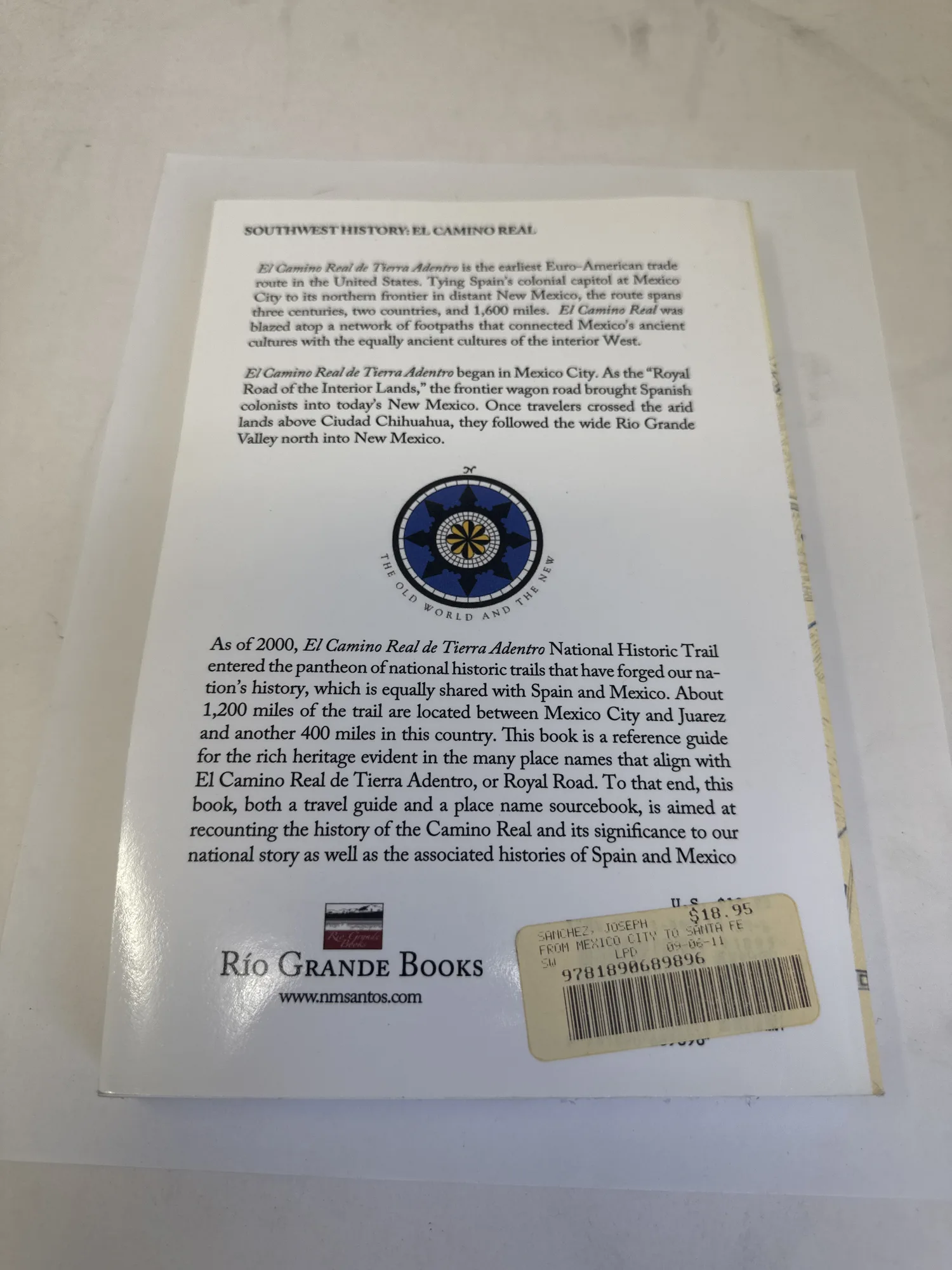 Back cover of From Mexico City to Santa Fe showing the Rio Grande Books compass rose logo, description of El Camino Real de Tierra Adentro as a National Historic Trail, ISBN 978-1-890689-89-6, and $18.95 price sticker. The text describes the road as spanning three centuries, two countries, and 1,600 miles. Photographed at the New Mexico Literacy Project sorting desk in Albuquerque.