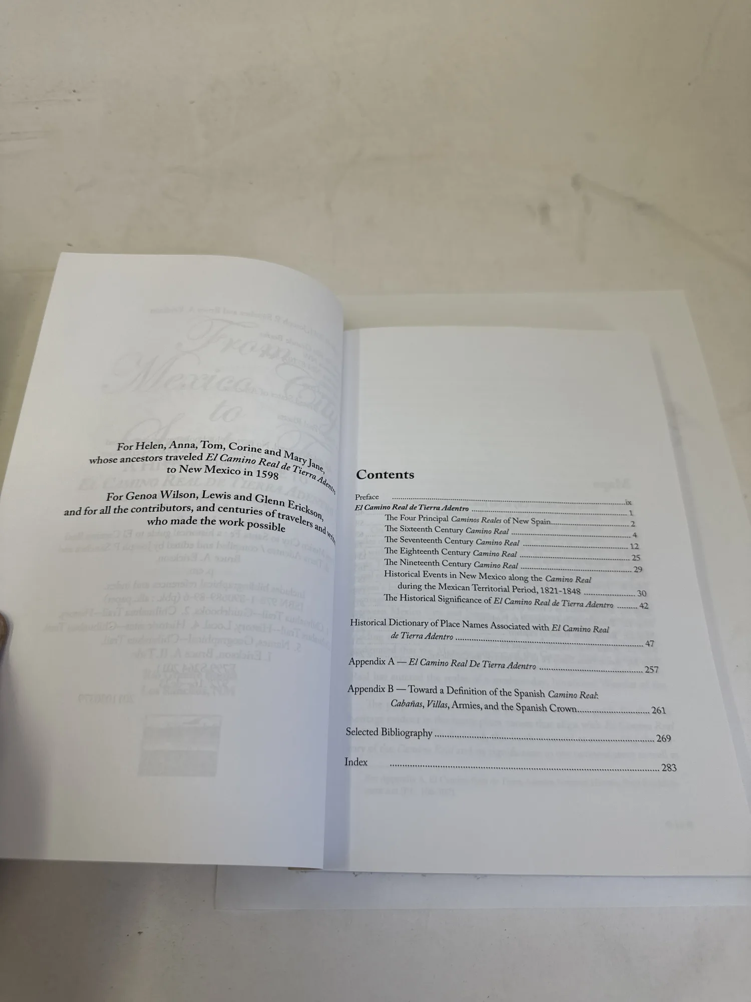 Table of contents and dedication page of From Mexico City to Santa Fe by Sánchez and Erickson, showing chapter structure organized by century from the sixteenth through the nineteenth, plus appendixes on place names and colonial definitions. The dedication reads: For Helen, Anna, Tom, Corine and Mary June, whose ancestors traveled El Camino Real de Tierra Adentro to New Mexico in 1598. Photographed at the New Mexico Literacy Project sorting desk in Albuquerque.