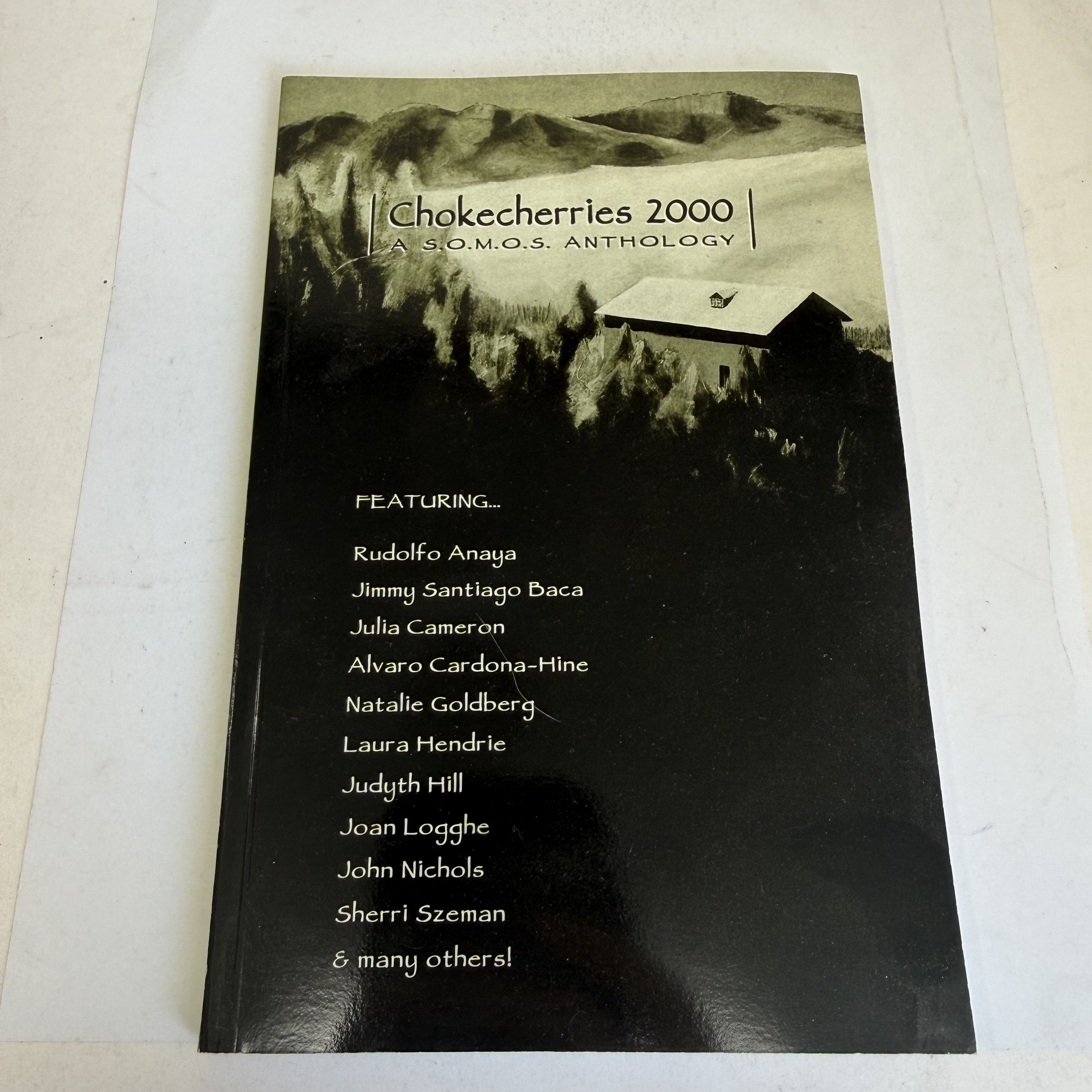 Front cover of Chokecherries 2000: A S.O.M.O.S. Anthology, featuring Barbara MacCauley's acrylic painting Distant Farm — a dark mountain landscape with a white house — and white text listing contributors including Rudolfo Anaya, Jimmy Santiago Baca, Julia Cameron, Natalie Goldberg, John Nichols, and others