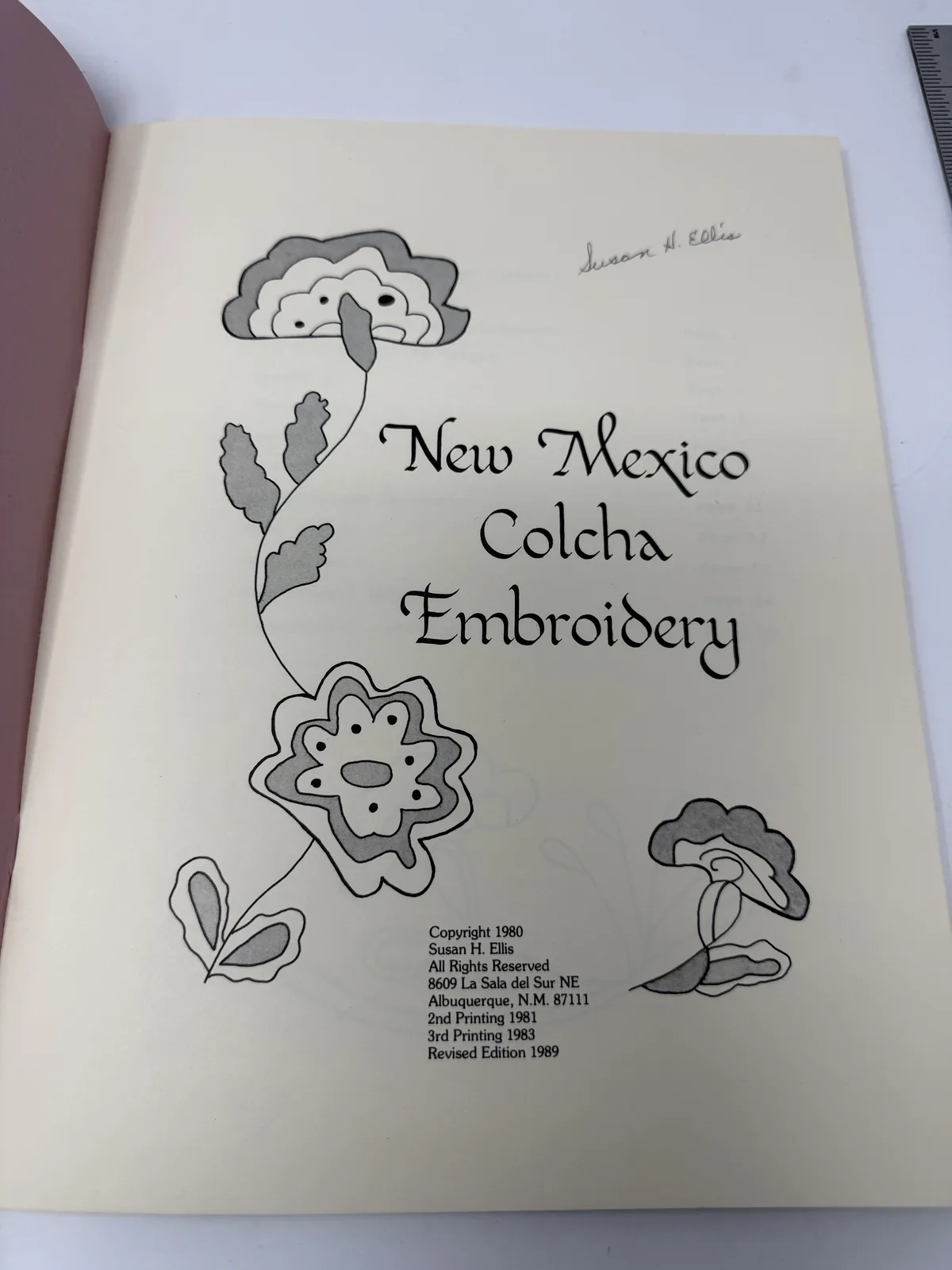 Hand-lettered title page of New Mexico Colcha Embroidery by Susan H. Ellis with drawn colcha flower motifs and the Albuquerque imprint, signed by the author, photographed at New Mexico Literacy Project