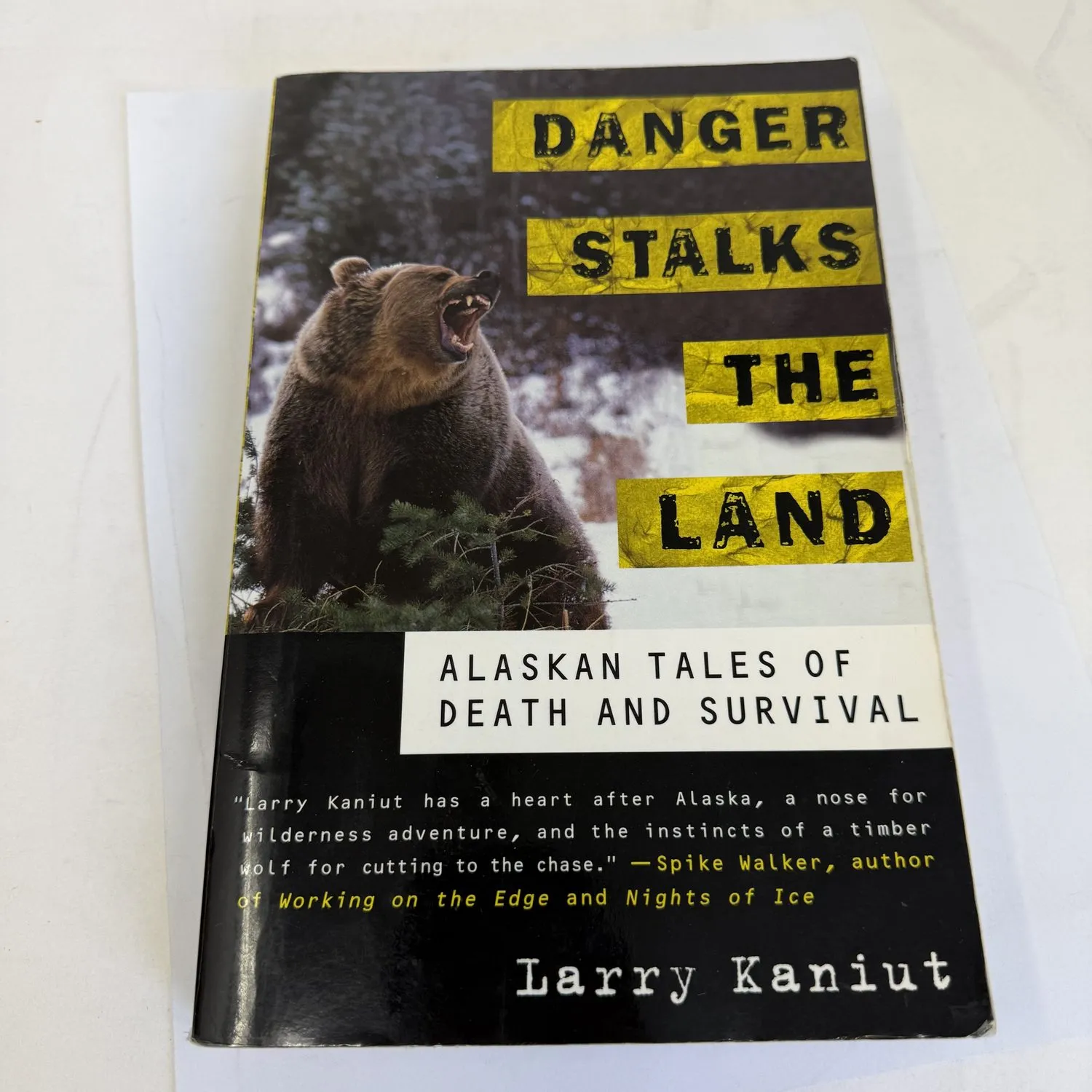 Front cover of Danger Stalks the Land Alaskan Tales of Death and Survival by Larry Kaniut, St. Martin's Griffin first edition November 1999, showing a roaring grizzly bear in snowy Alaskan wilderness with yellow and black title lettering and a Spike Walker blurb. Found in a New Mexico estate cleanout by the New Mexico Literacy Project.