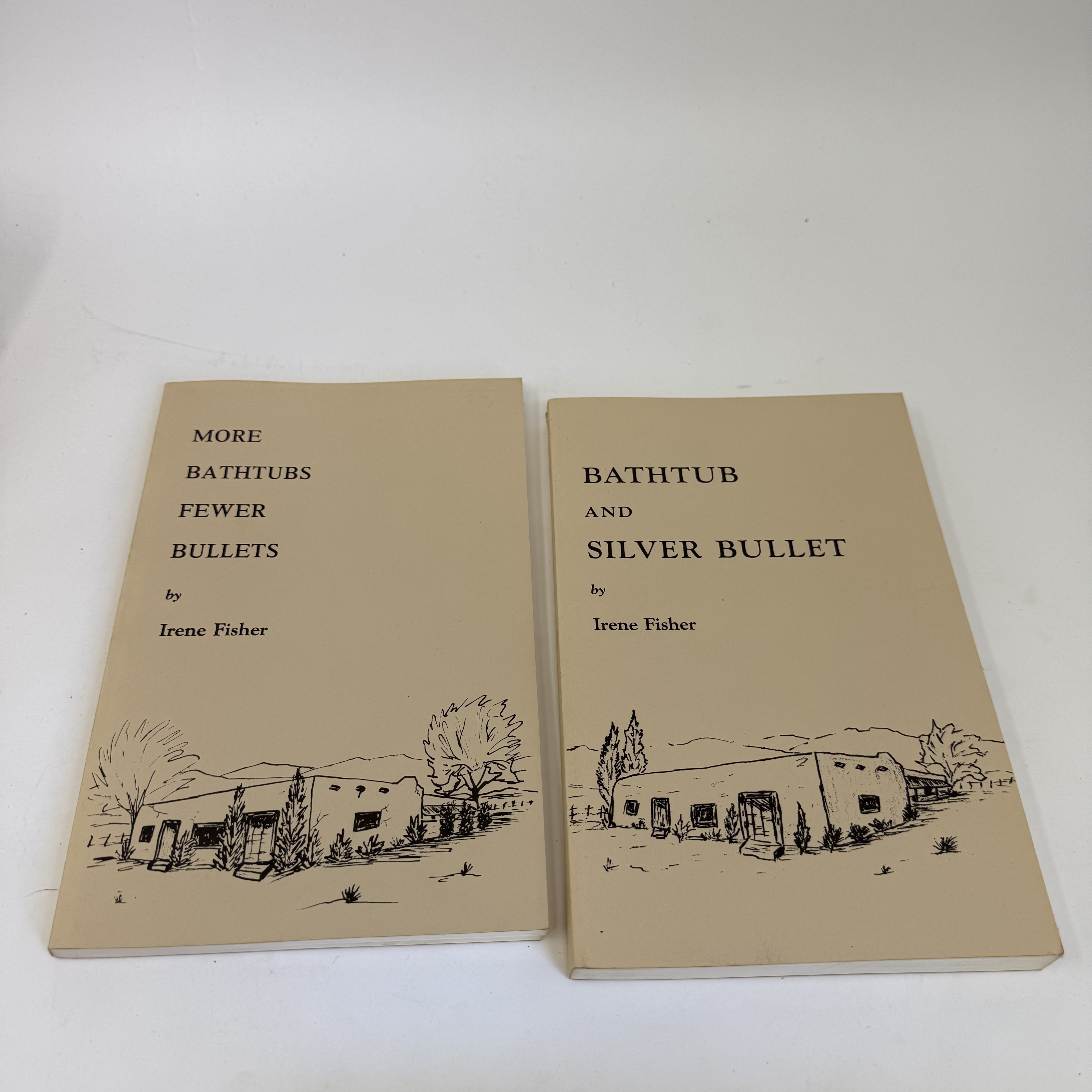 Two cream-paper trade paperback books side by side: 'Bathtub and Silver Bullet' on the left and 'More Bathtubs Fewer Bullets' on the right, both by Irene Fisher. The matched pair share a coordinated design — pen-and-ink illustrations of adobe houses with surrounding cottonwood and chile-string vegetation on cream-colored cardstock covers. The Albuquerque Historical Society and Tumbleweed Press Placitas imprint is visible on the cover of the first volume.