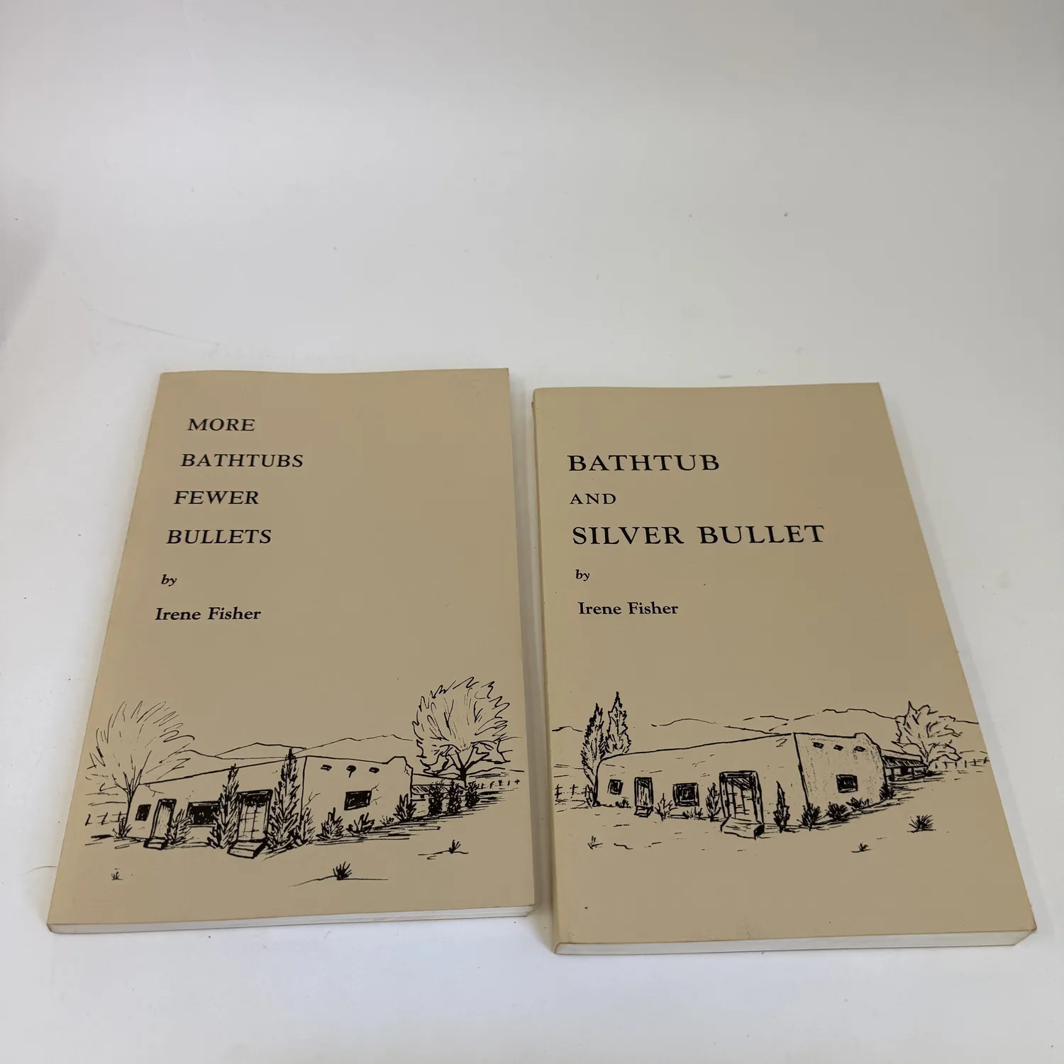 A pair of older paperback books titled Bathtub and Silver Bullet and More Bathtubs Fewer Bullets by NM-frontier-era memoirist Irene Fisher, lying on a wooden surface.