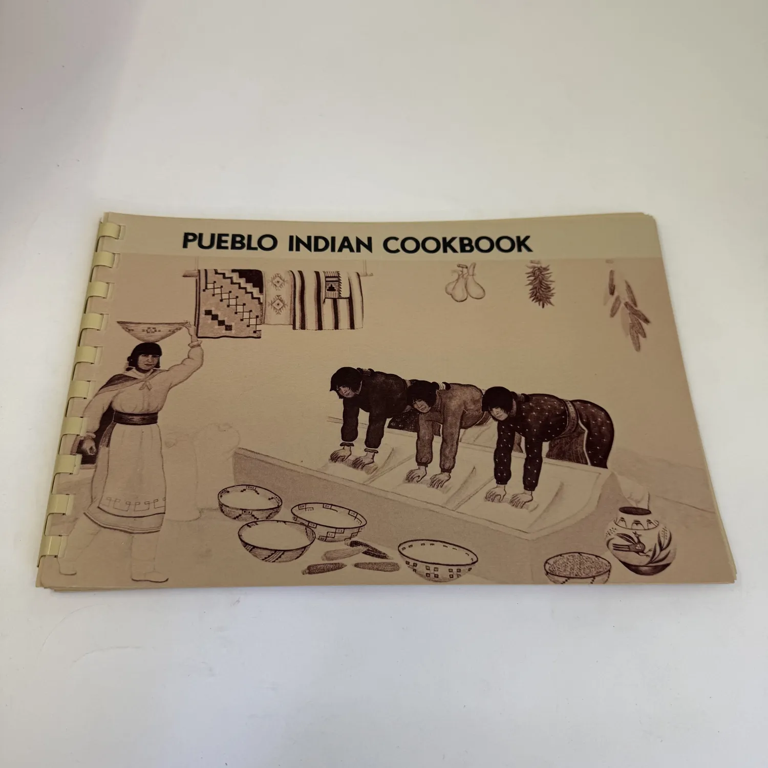 A signed Pueblo Indian Cookbook by Phyllis Hughes lying on a wooden surface with a Museum of New Mexico Press imprint visible on the cover.