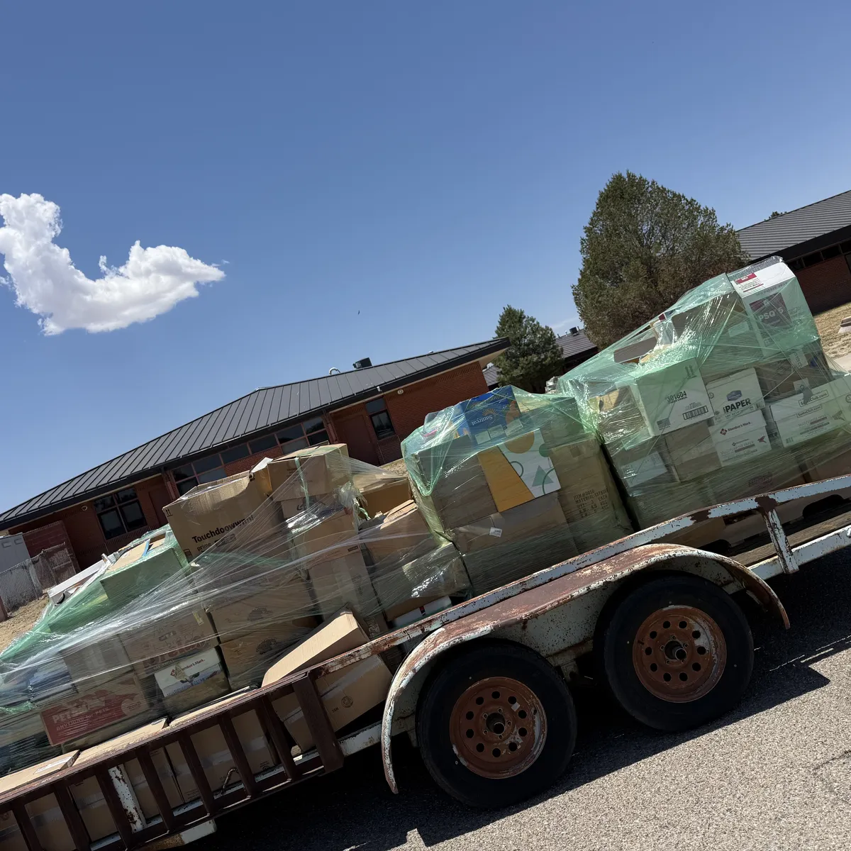 A utility trailer loaded with shrink-wrapped pallets of excess books outside an Estancia, New Mexico school during a free New Mexico Literacy Project school library cleanout, June 2026.