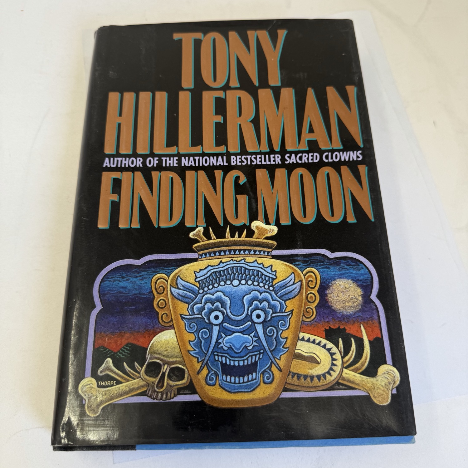 Front cover and dust jacket of Finding Moon by Tony Hillerman — first edition HarperCollins 1995, black background with colorful Asian-themed illustration featuring blue demon mask, skull and crossbones, and gold accents