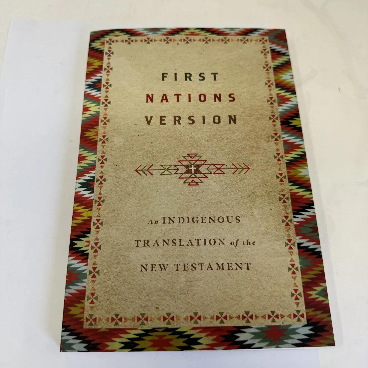 Front cover of First Nations Version: An Indigenous Translation of the New Testament — red, yellow, black and green Native American diamond pattern on dark background, InterVarsity Press 2021