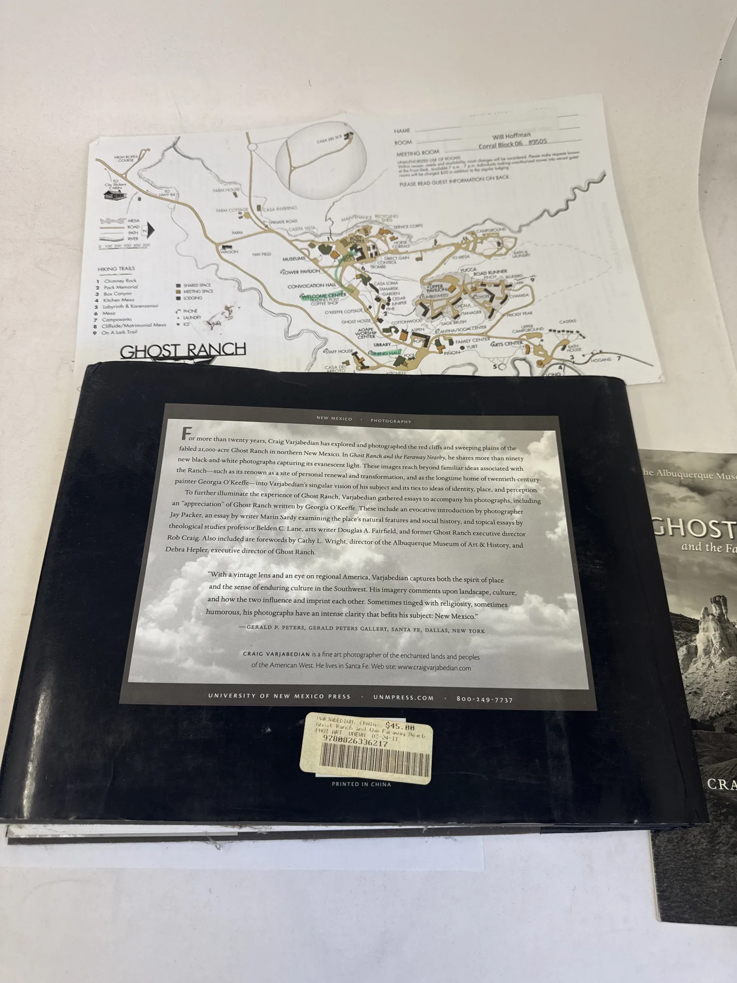 Back cover of Ghost Ranch and the Faraway Nearby showing publisher description of Craig Varjabedian landscape photography, University of New Mexico Press imprint, and original price sticker. Photographed at the New Mexico Literacy Project sorting desk in Albuquerque.
