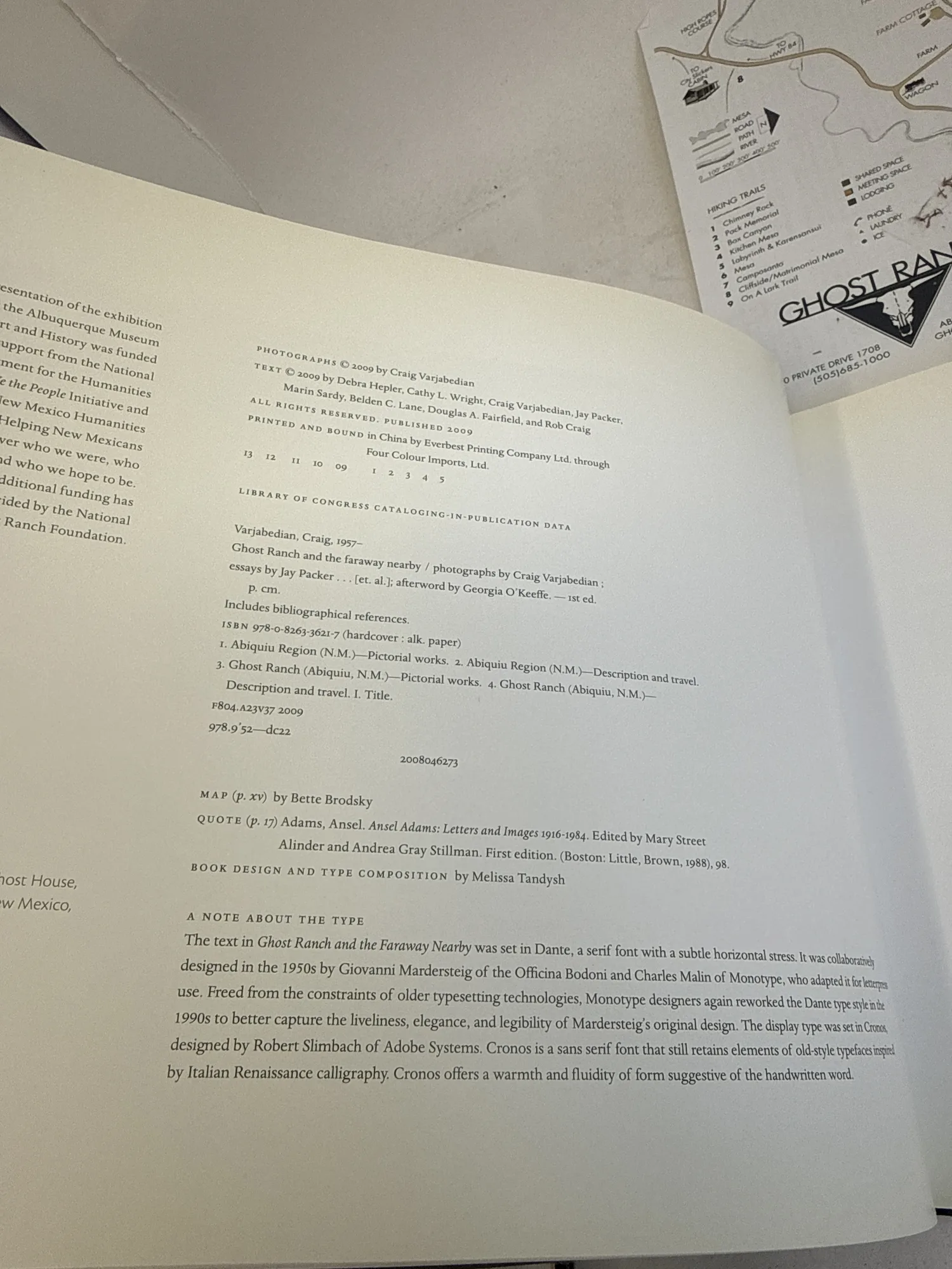 Copyright and colophon page of Ghost Ranch and the Faraway Nearby showing ISBN 978-0-8263-3927-7, Library of Congress cataloging data, contributor credits, and typography notes about Dante and Cronos typefaces. Photographed at the New Mexico Literacy Project sorting desk in Albuquerque.