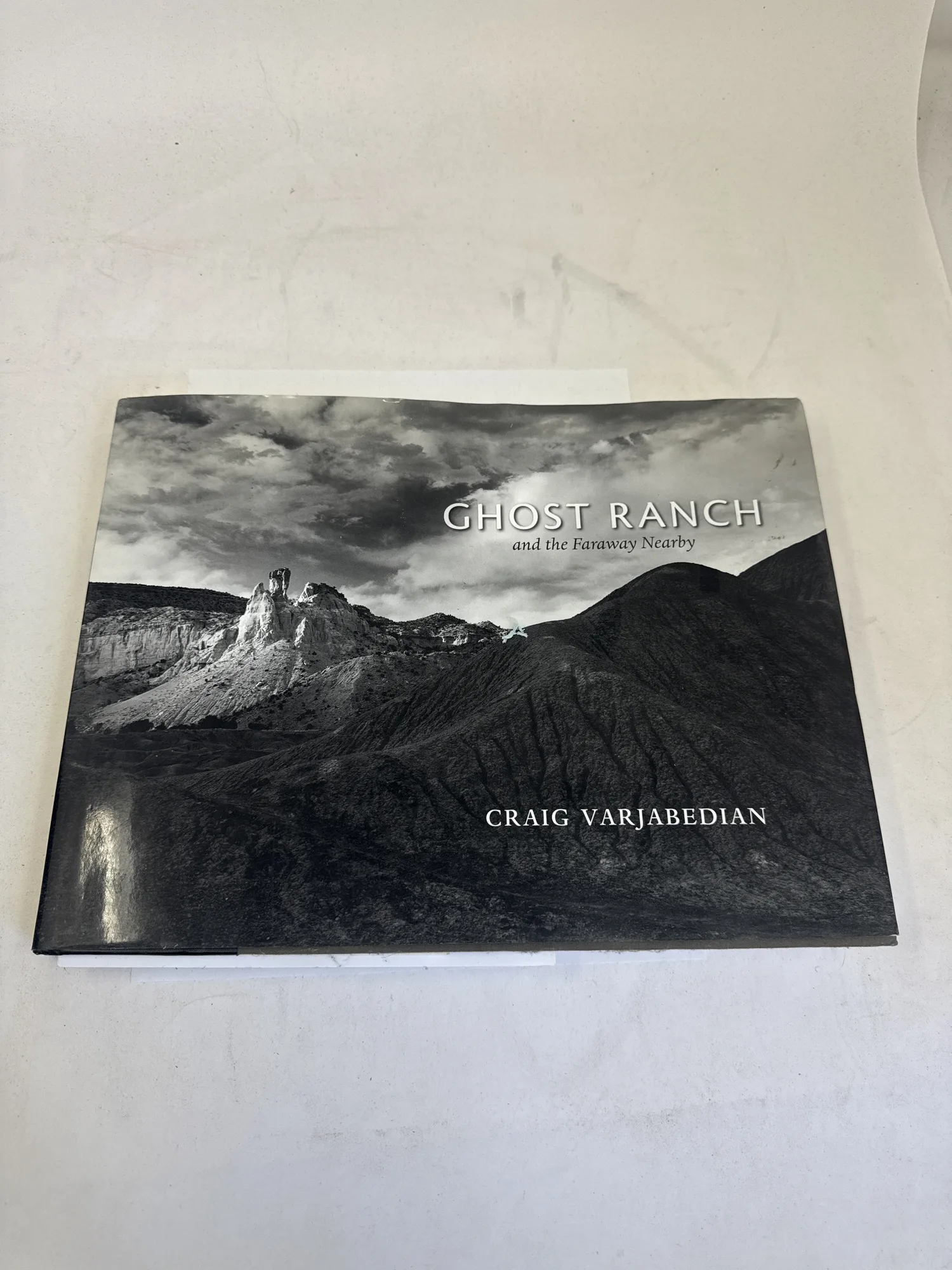 Front cover of Ghost Ranch and the Faraway Nearby by Craig Varjabedian, showing a dramatic black-and-white photograph of Ghost Ranch cliffs against towering clouds, published by University of New Mexico Press 2009. Photographed at the New Mexico Literacy Project sorting desk in Albuquerque.
