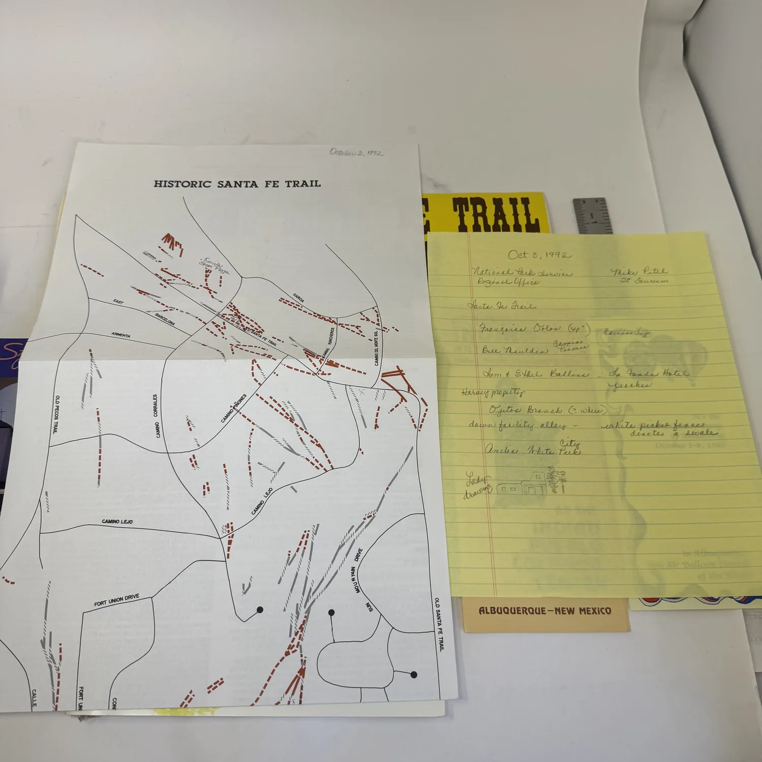 Historic Santa Fe Trail map dated October 3 1992 showing the Old Pecos Trail route through Santa Fe with street-level detail including Fort Union Drive, Camino Lejo, and Old Santa Fe Trail, wagon rut locations marked in red dashes, alongside yellow legal-pad field notes referencing National Park Service Regional Office, La Fonda Hotel, and Amelia White Park. Primary research documents from an Albuquerque estate donation to the New Mexico Literacy Project.