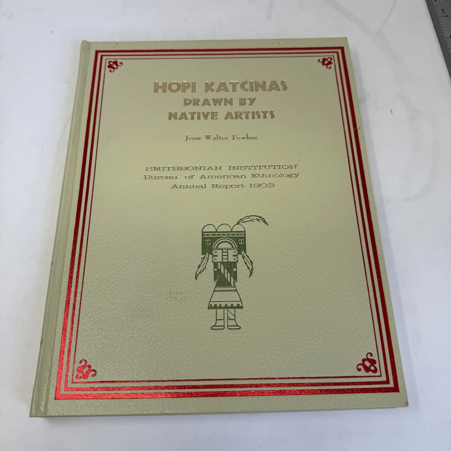 Cover of Hopi Katcinas Drawn by Native Artists by Jesse Walter Fewkes — sage cloth binding with red border and gold lettering, kachina figure illustration, Smithsonian Institution Bureau of American Ethnology Annual Report 1903, Rio Grande Press reprint. Photographed at the New Mexico Literacy Project in Albuquerque.