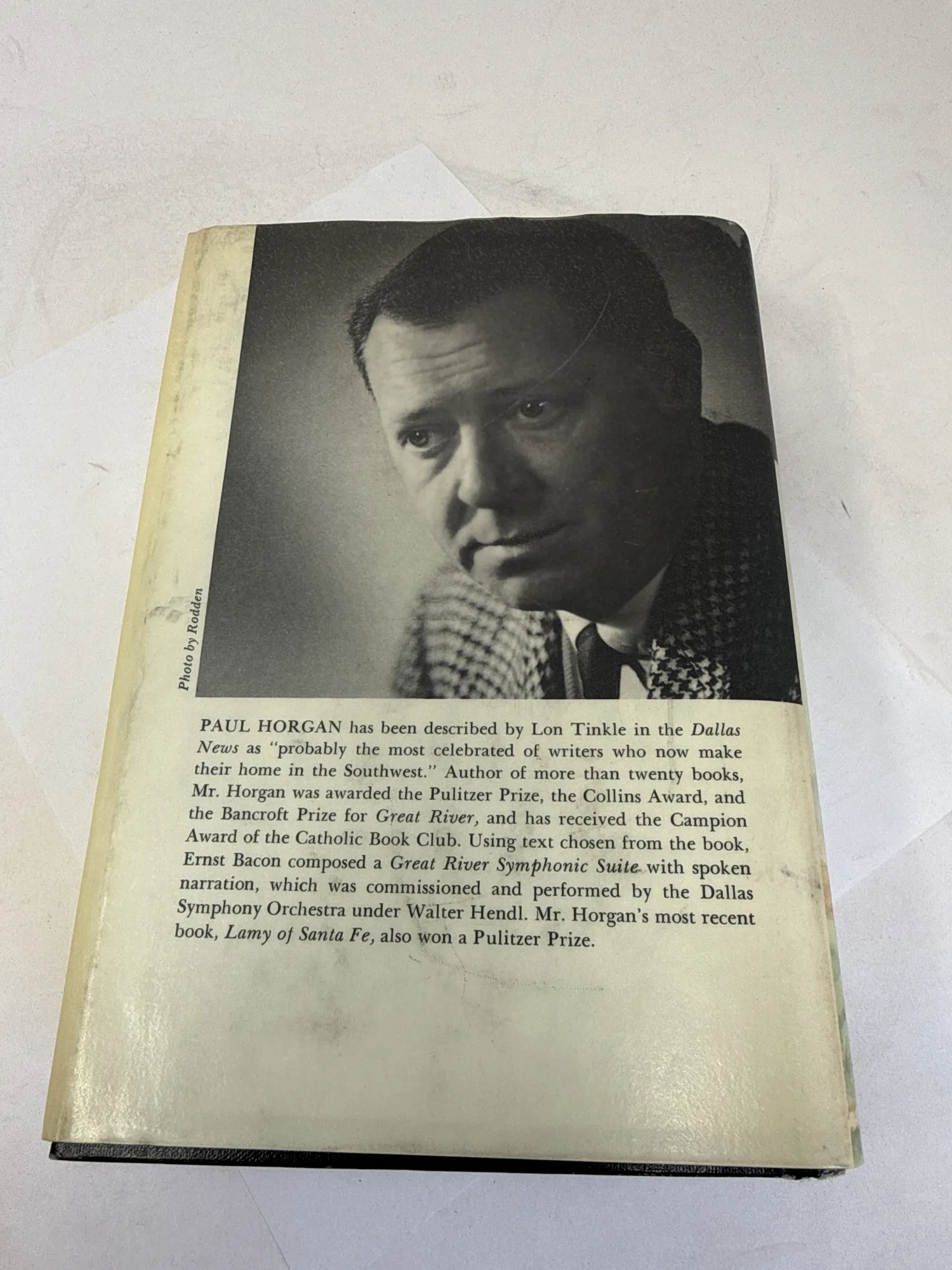 Back flap of Great River dust jacket showing author photo of Paul Horgan by Rodden in houndstooth jacket, biographical note mentioning Pulitzer Prize, Bancroft Prize, Collins Award, Campion Award, Ernst Bacon Great River Symphonic Suite performed by Dallas Symphony Orchestra, and Lamy of Santa Fe Pulitzer Prize. Photographed at the New Mexico Literacy Project sorting desk in Albuquerque.