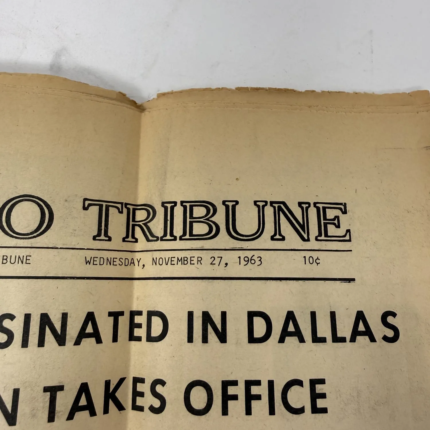 Close-up of the Toronto Tribune masthead showing the newspaper name, Wednesday November 27 1963 date, and 10 cent price, with the top of the assassination headlines visible below. Yellowed newsprint from a small-town Ohio River newspaper preserved for sixty years.