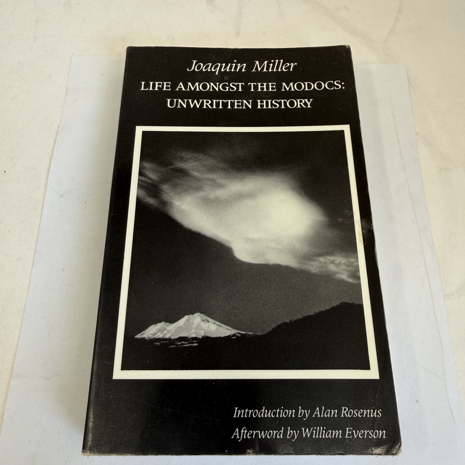 Front cover of Life Amongst the Modocs Unwritten History by Joaquin Miller, Urion Press reprint. Black cover with a white-framed black-and-white photograph of Mount Shasta with dramatic cloud formation by Robert McKenzie. Joaquin Miller name in italic white lettering. Originally published 1873, this scholarly reprint includes an introduction by Alan Rosenus and afterword by William Everson. Found in a New Mexico estate cleanout by the New Mexico Literacy Project.