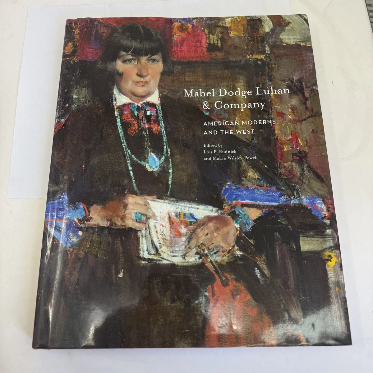 Cover of Mabel Dodge Luhan and Company: American Moderns and the West, published by Museum of New Mexico Press 2016, showing a painting of Mabel Dodge Luhan seated and reading while wearing turquoise jewelry — photographed by Josh Eldred at the New Mexico Literacy Project workspace