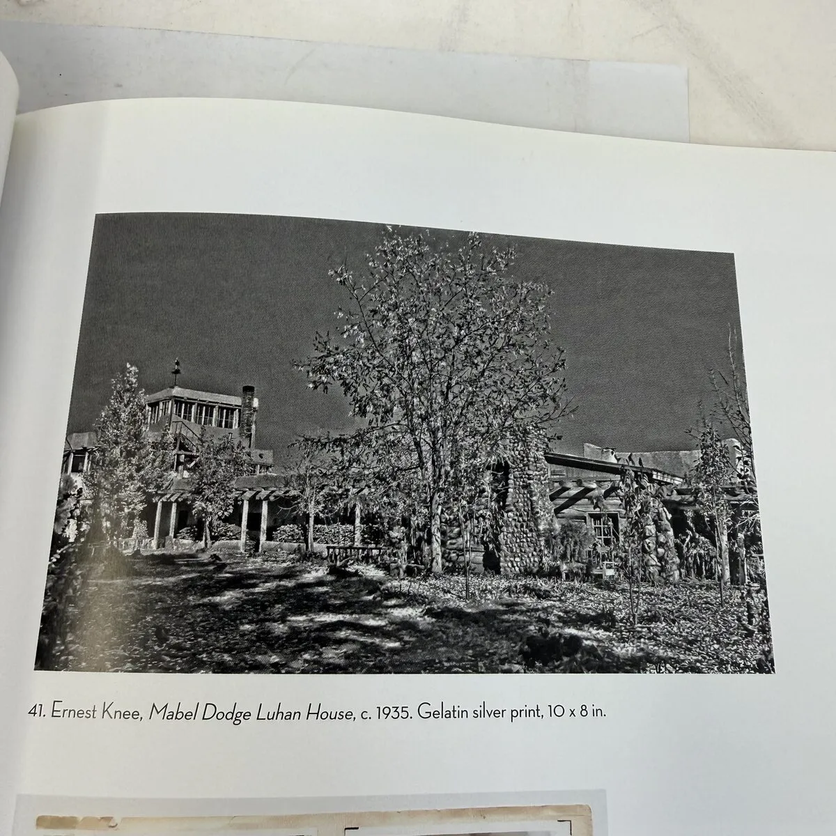 Ernest Knee exterior photograph of the Mabel Dodge Luhan House circa 1935, gelatin silver print showing adobe walls, trees, and pergola in Taos New Mexico — from Mabel Dodge Luhan and Company, photographed by Josh Eldred
