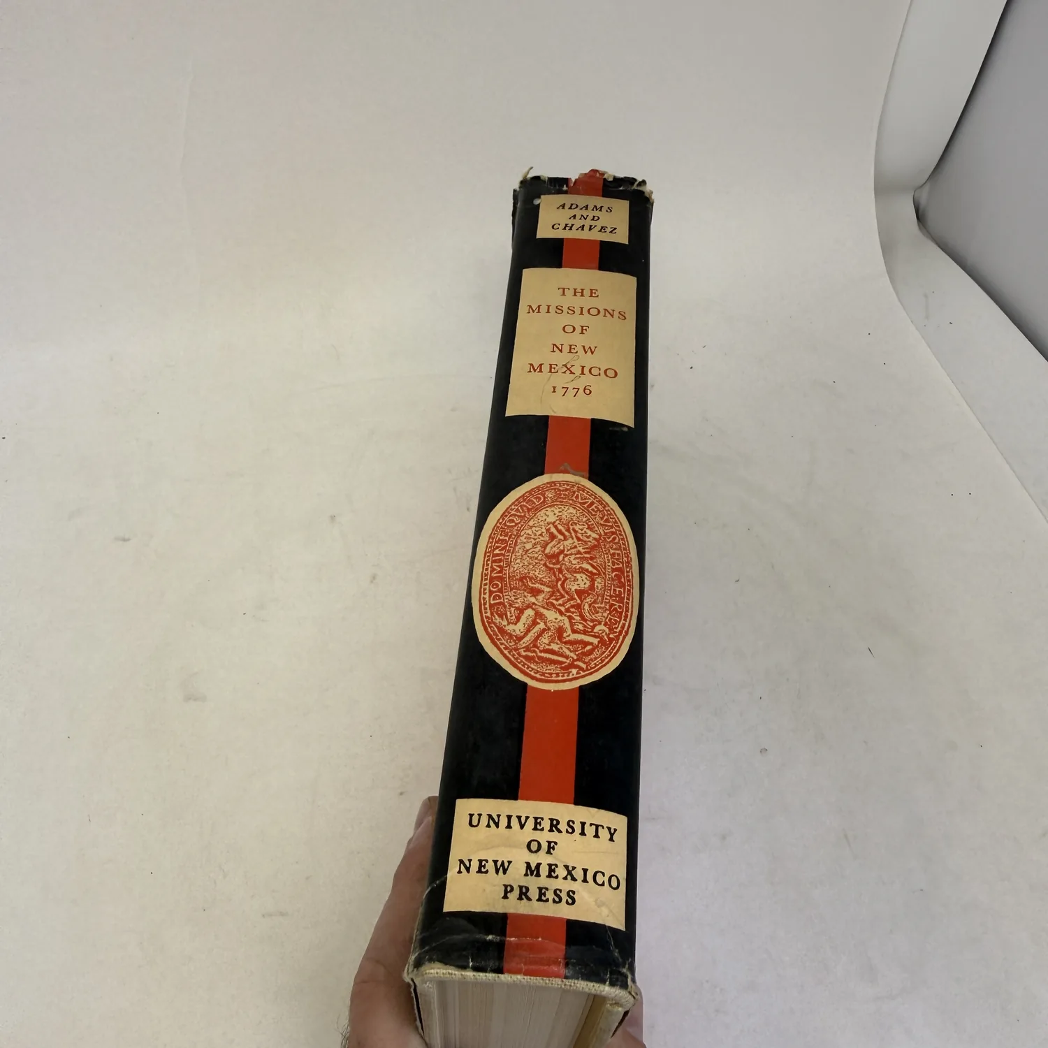 Spine of the Missions of New Mexico, 1776 dust jacket, black with a red stripe, with labels reading Adams and Chavez and University of New Mexico Press and a red oval seal, photographed at New Mexico Literacy Project