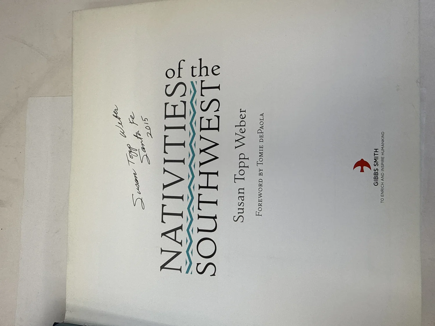 Title page of Nativities of the Southwest signed by Susan Topp Weber in ink reading Susan Topp Weber Santa Fe 2015, with Gibbs Smith publisher logo and foreword credit to Tomie dePaola. Photographed at the New Mexico Literacy Project sorting desk in Albuquerque.