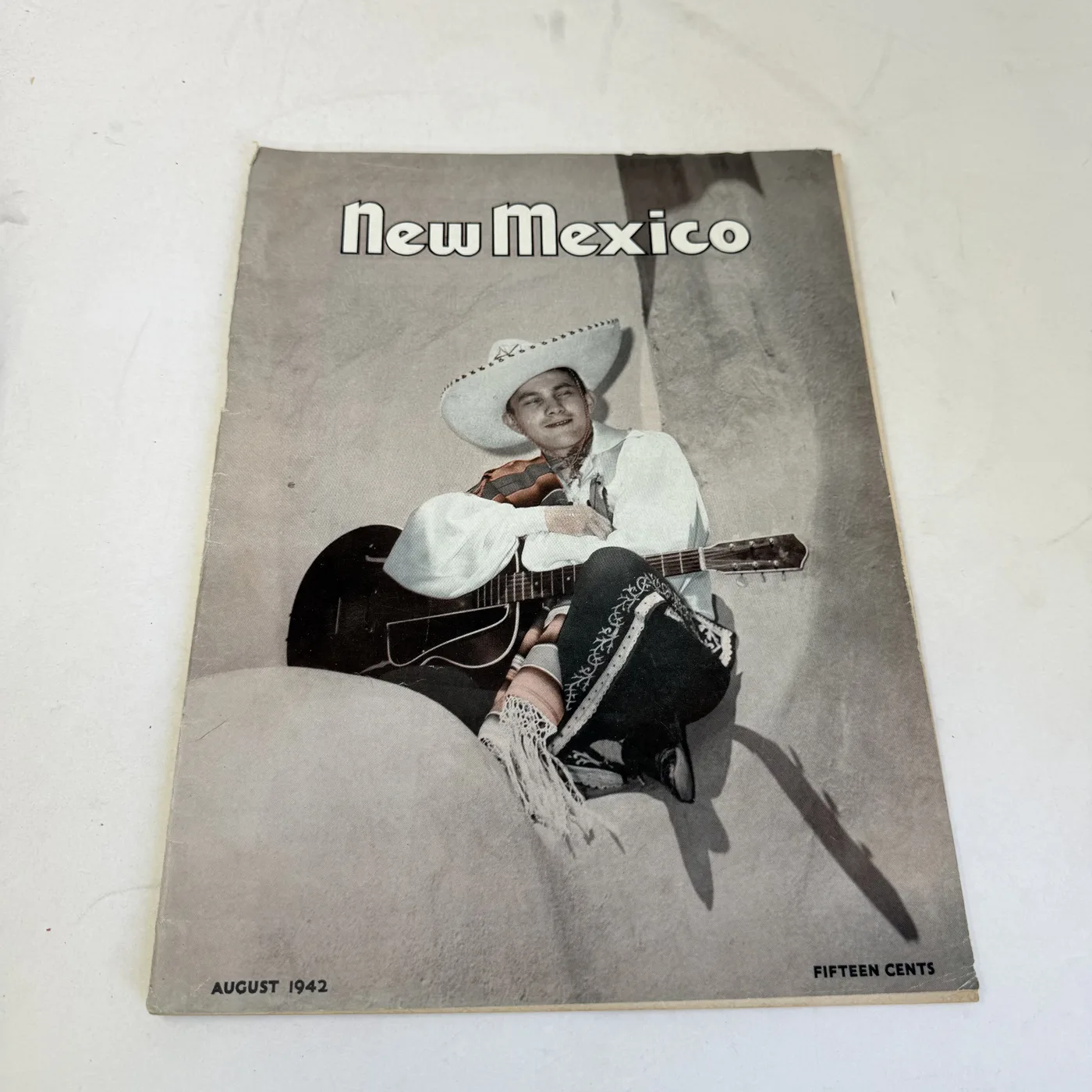 New Mexico Magazine August 1942 cover: cowboy in a white hat playing guitar, fifteen cents — photographed at New Mexico Literacy Project