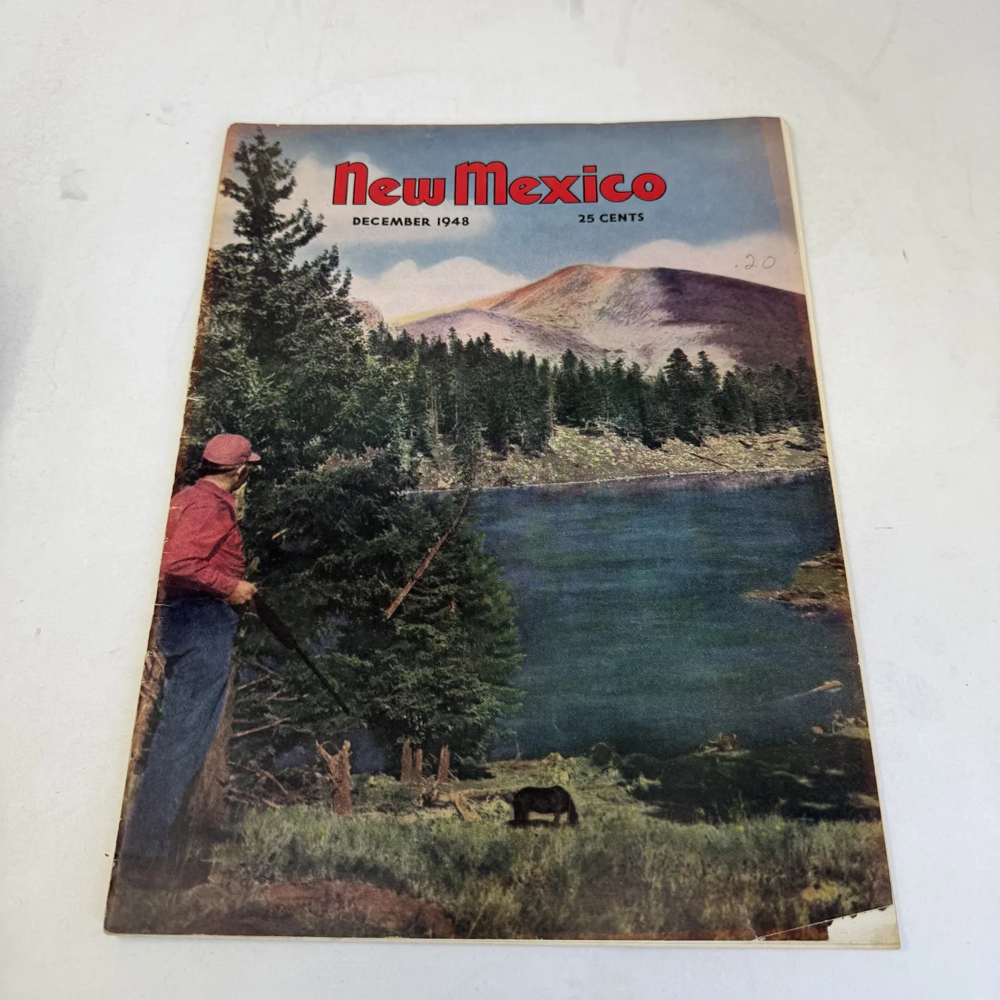New Mexico Magazine December 1948 cover: fisherman in a red shirt working a meadow stream below forested hills — photographed at New Mexico Literacy Project