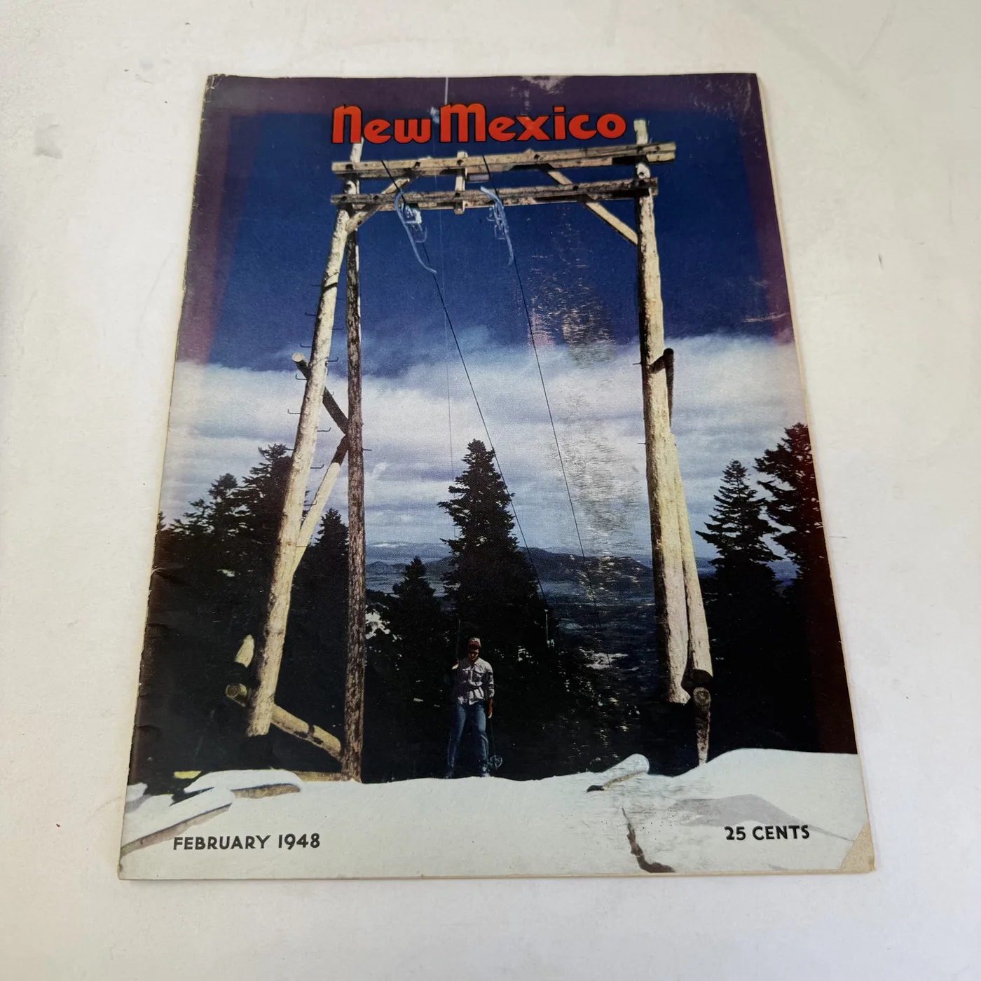 New Mexico Magazine February 1948 cover: early chairlift with single chairs hanging from a timber log tower above a snowy slope, twenty-five cents — photographed at New Mexico Literacy Project