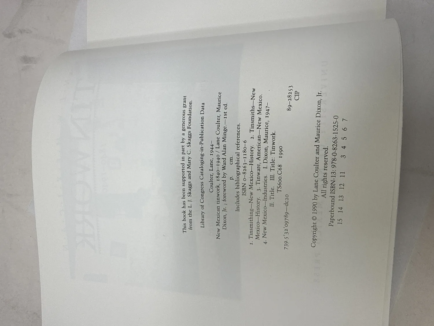 Copyright page of New Mexican Tinwork 1840-1940 showing first edition confirmed by number line 15 14 13 12 11 and 3 4 5 6 7, Copyright 1990 by Lane Coulter and Maurice Dixon Jr., ISBN 0-8263-1180-6, Library of Congress subject headings Tinsmithing New Mexico History and Tinsmiths New Mexico, supported by L.J. Skaggs and Mary C. Skaggs Foundation grant. Photographed at the New Mexico Literacy Project sorting desk in Albuquerque.