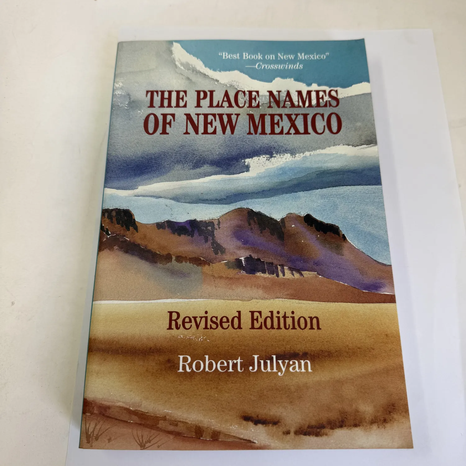 Front cover of The Place Names of New Mexico, Revised Edition by Robert Julyan — watercolor landscape illustration by Alice Peden showing New Mexico high desert with mesas and storm clouds, published by University of New Mexico Press