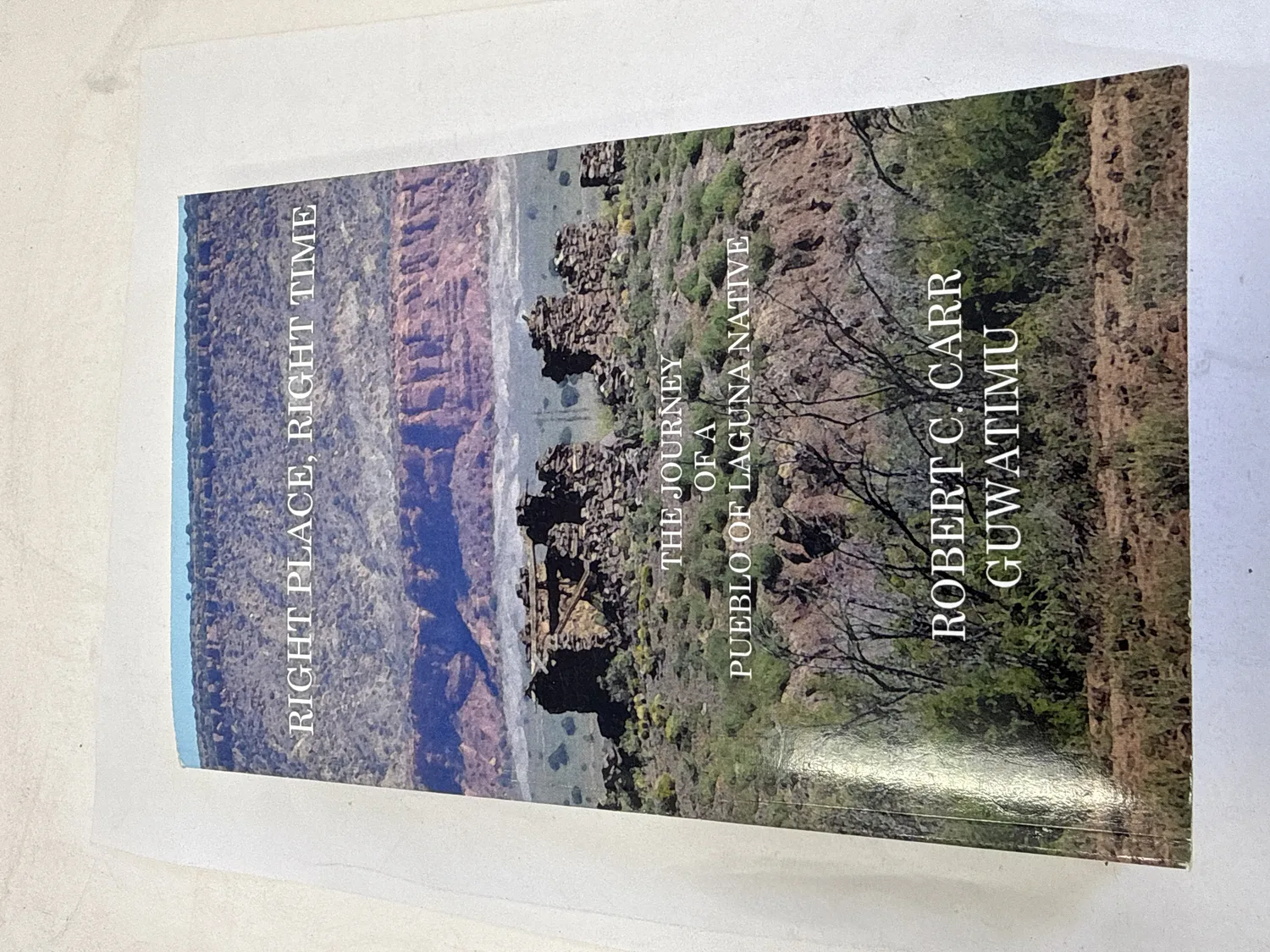 Front cover of Right Place, Right Time &mdash; The Journey of a Pueblo of Laguna Native by Robert C. Carr (Guwatimu), landscape photograph of ruins of family sheep camp at Skro kana against red rock mesas and desert scrub, All About Indians Press Albuquerque 2013. Photographed at the New Mexico Literacy Project sorting desk in Albuquerque.