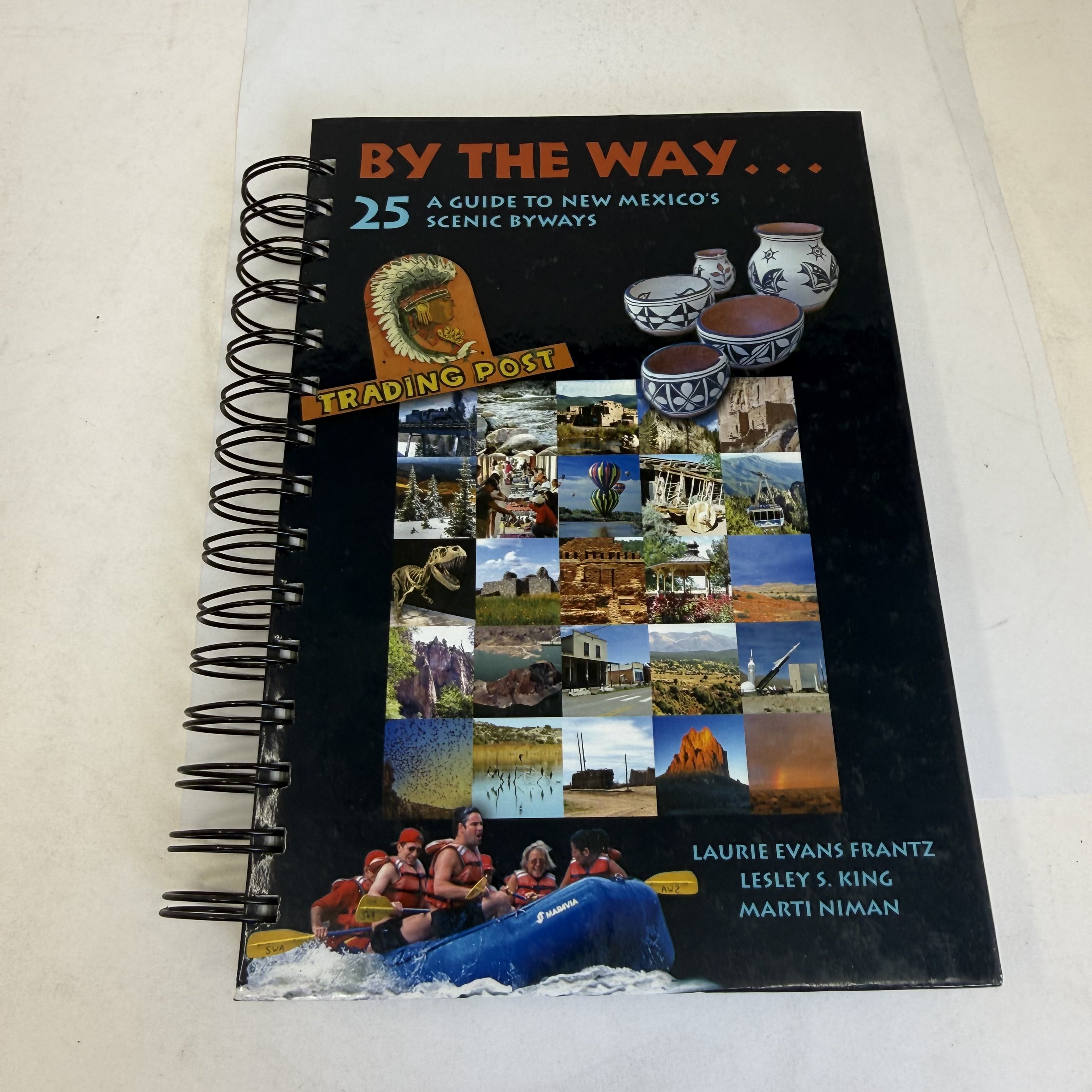 Front cover of By the Way 25 A Guide to New Mexico's Scenic Byways — spiral-bound travel guide with photo collage of NM landmarks including pottery, Trading Post sign, hot air balloons, ancient ruins, adobe churches, white water rafting, dinosaur skeleton, and Tent Rocks-style formations. Authors: Laurie Evans Frantz, Lesley S. King, Marti Niman. Published by New Mexico Magazine.