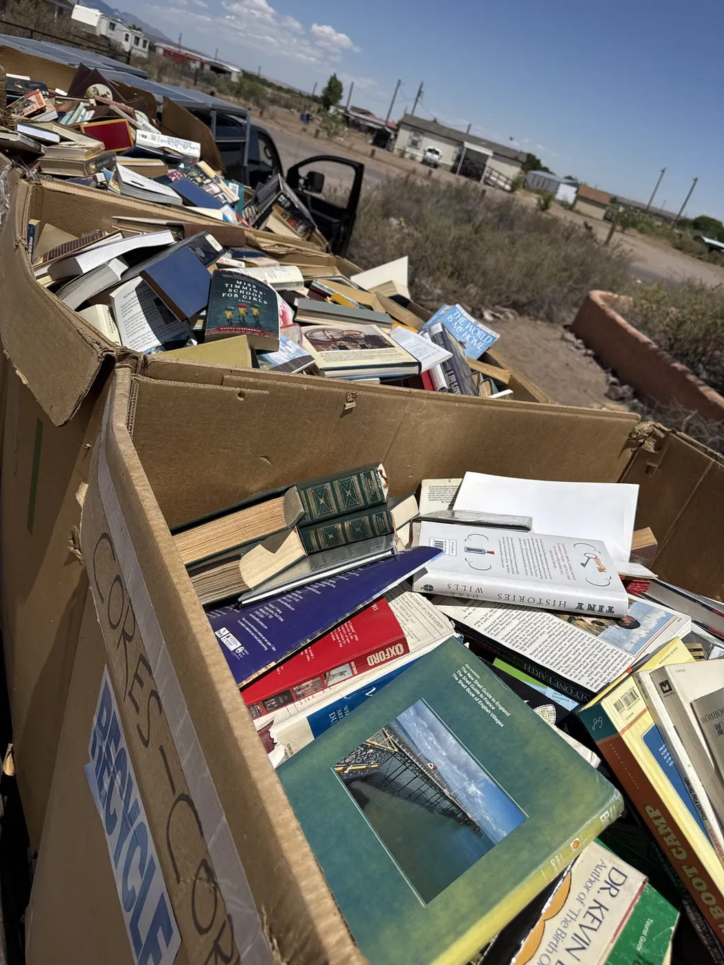 An open cardboard moving box inside the back of an NMLP pickup van, packed with hardcover books visible: medical and health-care references including a Dr. Kevin author title, leather-spine reference volumes, a Stanford-imprint textbook, religious bindings, and the corner of a Boscobel-related title — the diversity typical of an estate library.