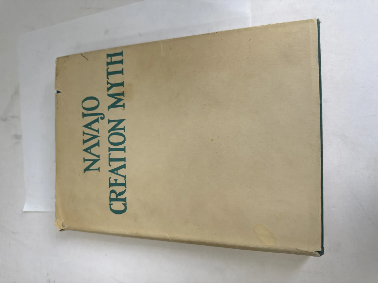 Dust jacket of Navajo Creation Myth by Hasteen Klah, 1942 first edition with green letterpress title on cream wrapper and green cloth binding visible at spine. Photographed at the New Mexico Literacy Project sorting desk in Albuquerque.