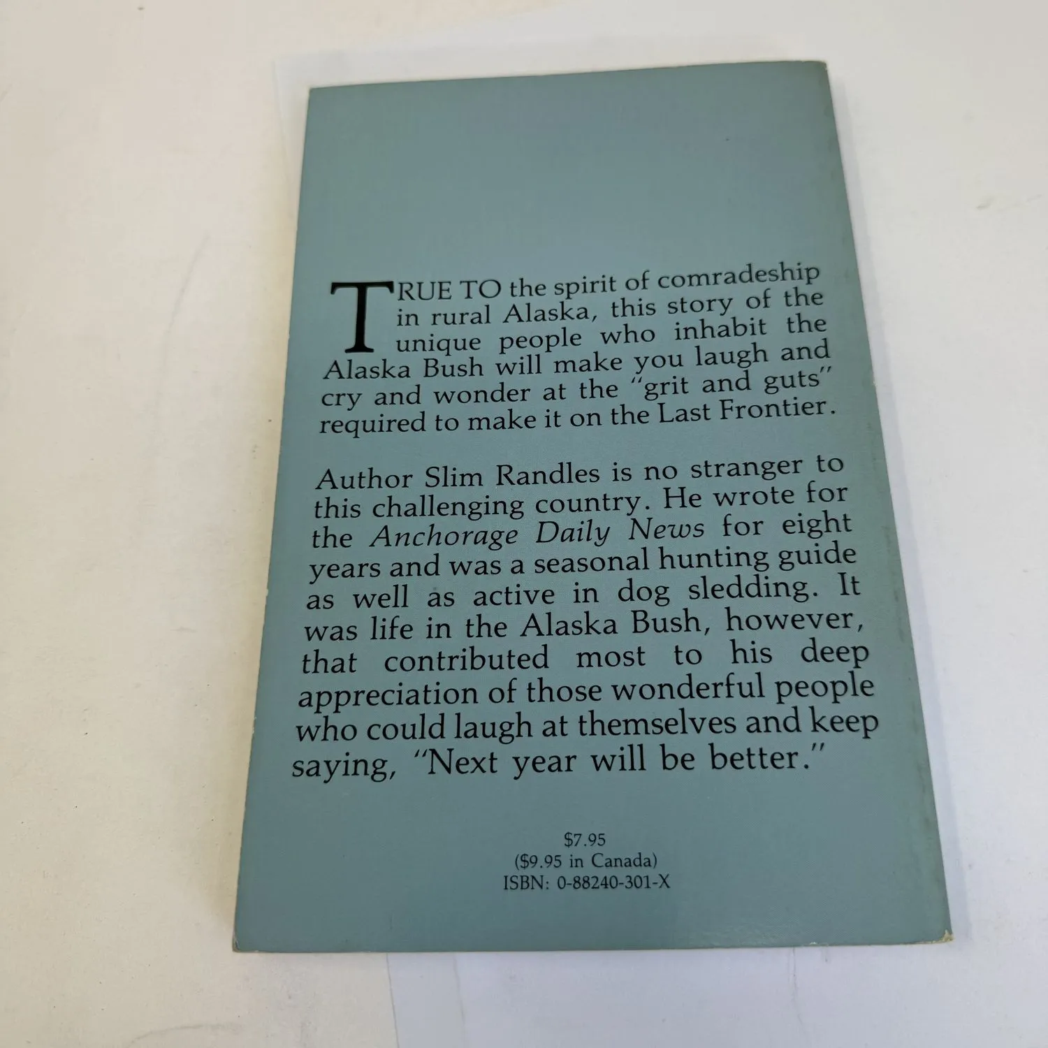 Back cover of The Long Dark by Slim Randles on light blue-gray stock, text reading True to the spirit of comradeship in rural Alaska this story of the unique people who inhabit the Alaska Bush will make you laugh and cry and wonder at the grit and guts required to make it on the Last Frontier. Author bio noting he wrote for the Anchorage Daily News for eight years was a seasonal hunting guide and active in dog sledding. $7.95 US $9.95 in Canada.
