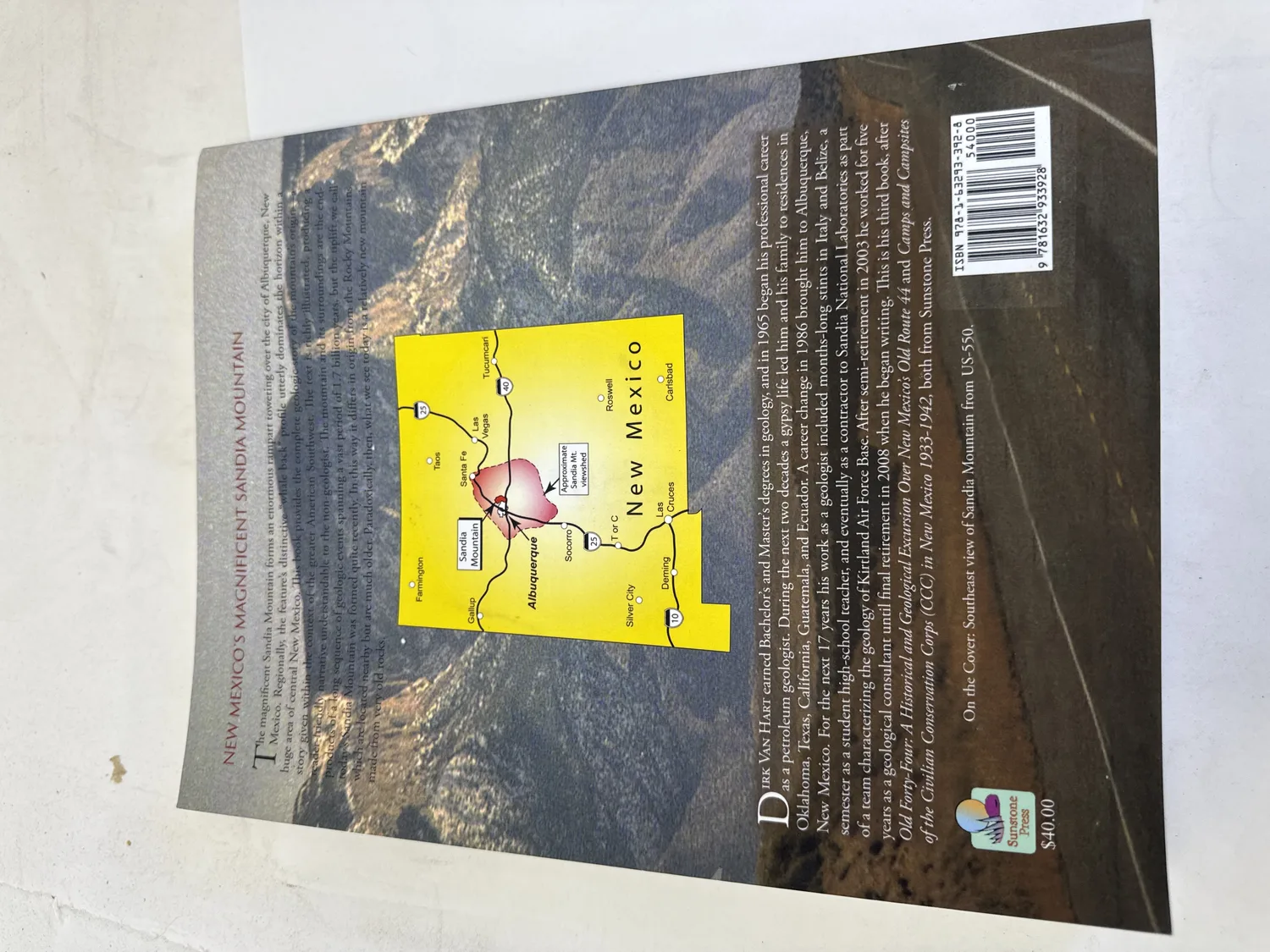 Back cover of New Mexico's Magnificent Sandia Mountain by Dirk Van Hart &mdash; author biography describing Sandia National Laboratories career, New Mexico location map with Albuquerque and Sandia Mountains marked, cover photograph credit, barcode with ISBN, $40.00 price. Photographed at the New Mexico Literacy Project sorting desk in Albuquerque.